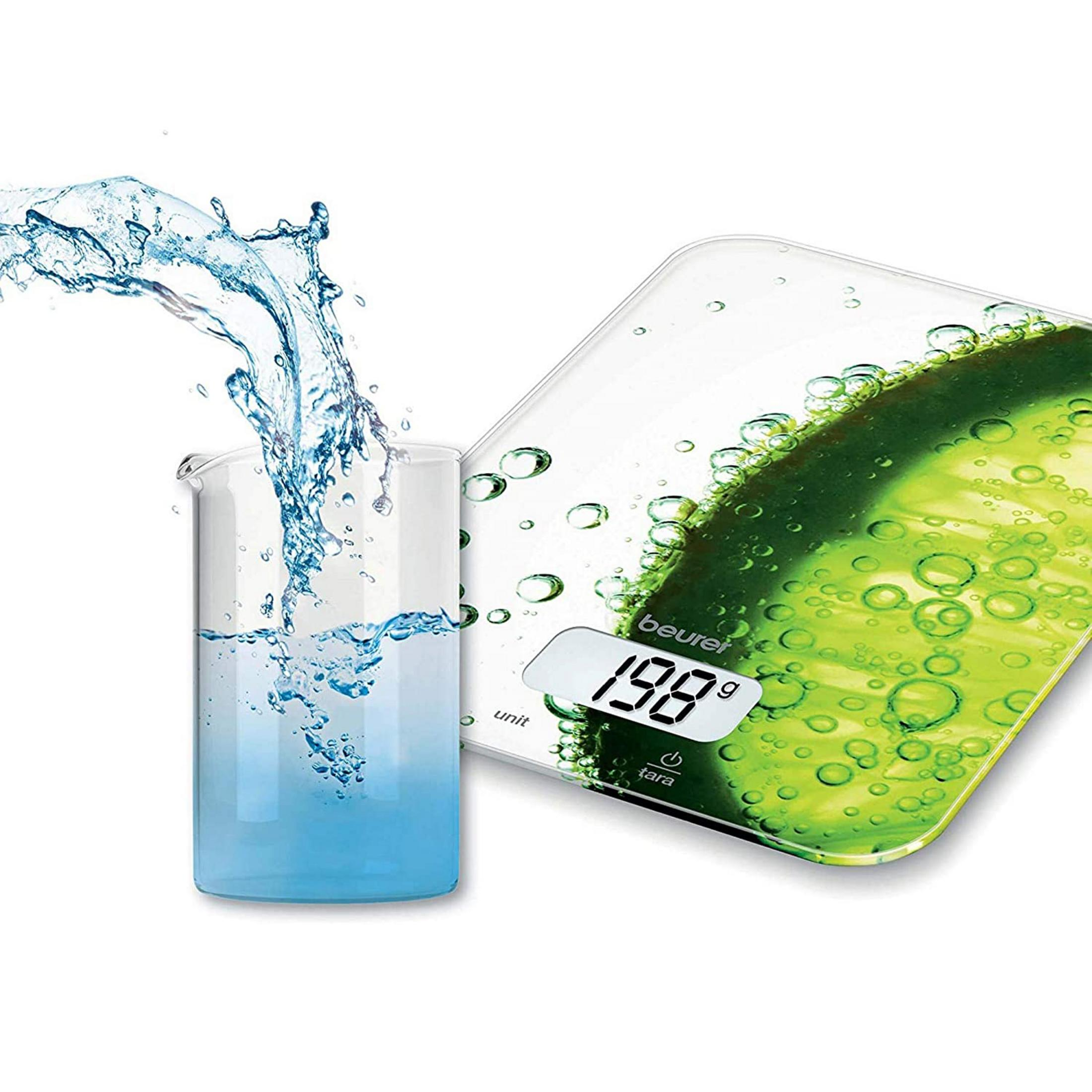 Ein Glas mit blauen Flüssigkeitsspritzern neben einer digitalen Küchenwaage mit Zitronenscheibendekor.