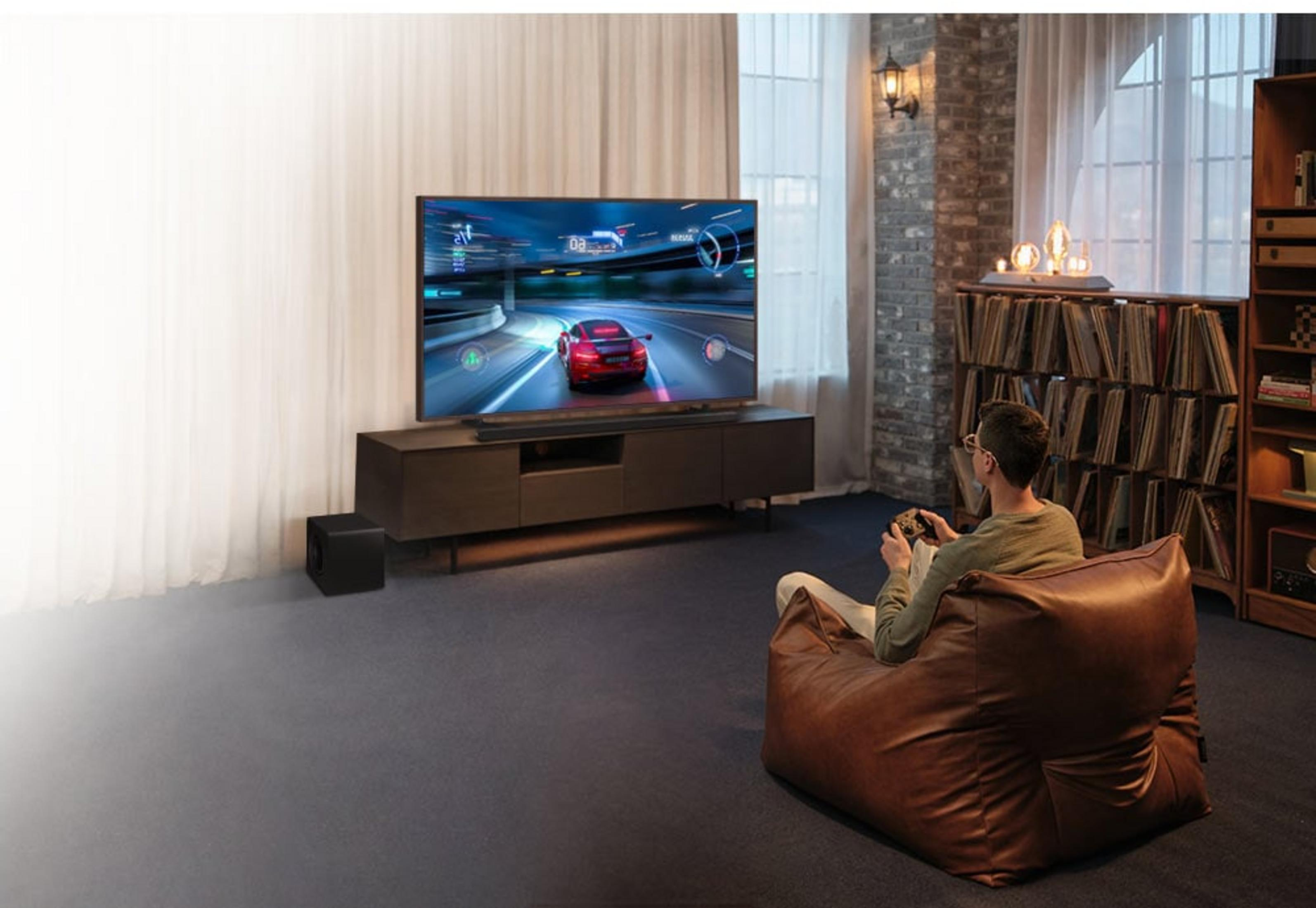 Man plays car racing game on large TV, sitting in brown leather beanbag chair.