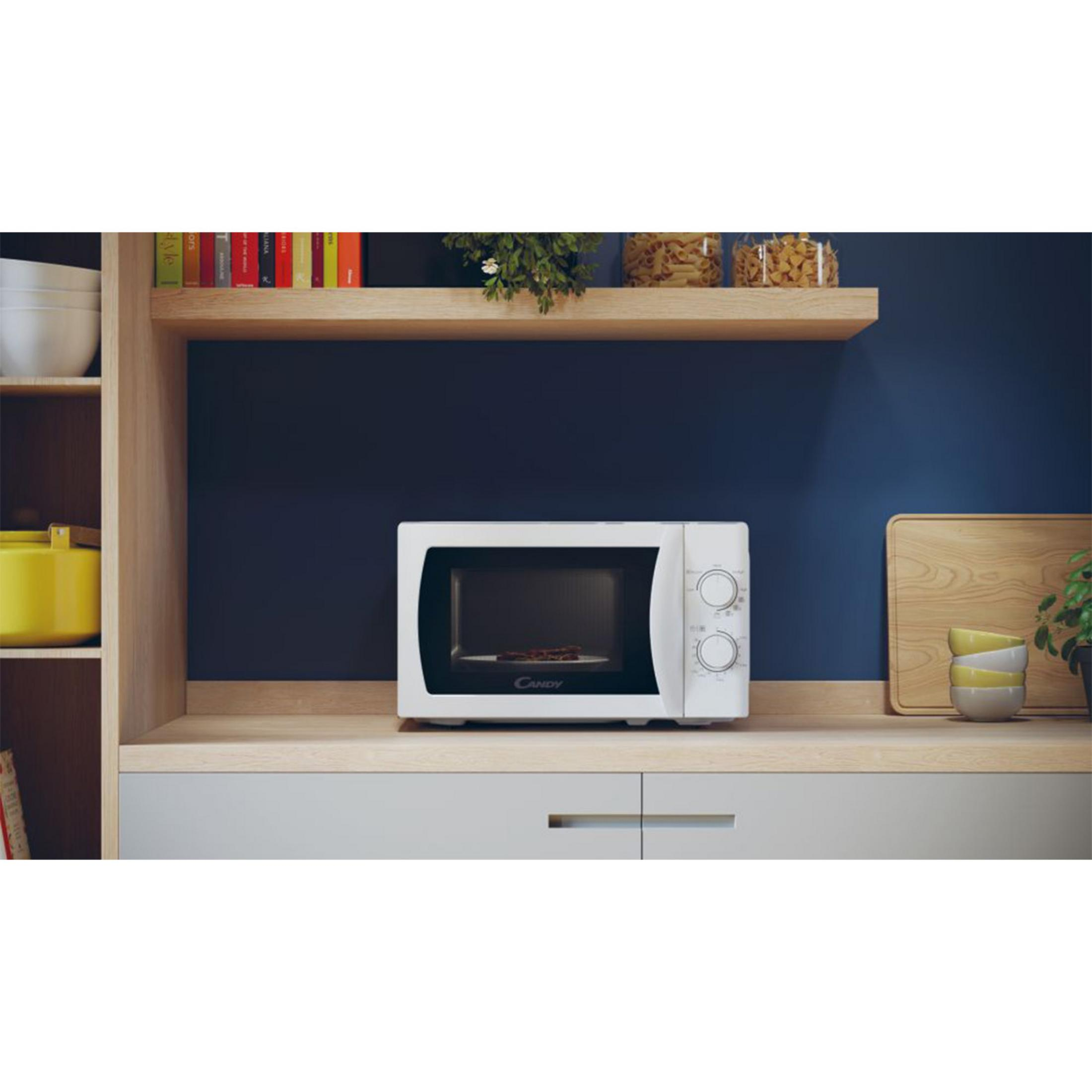 Een witte Candy magnetron staat op een houten aanrecht tegen een donkerblauwe muur.