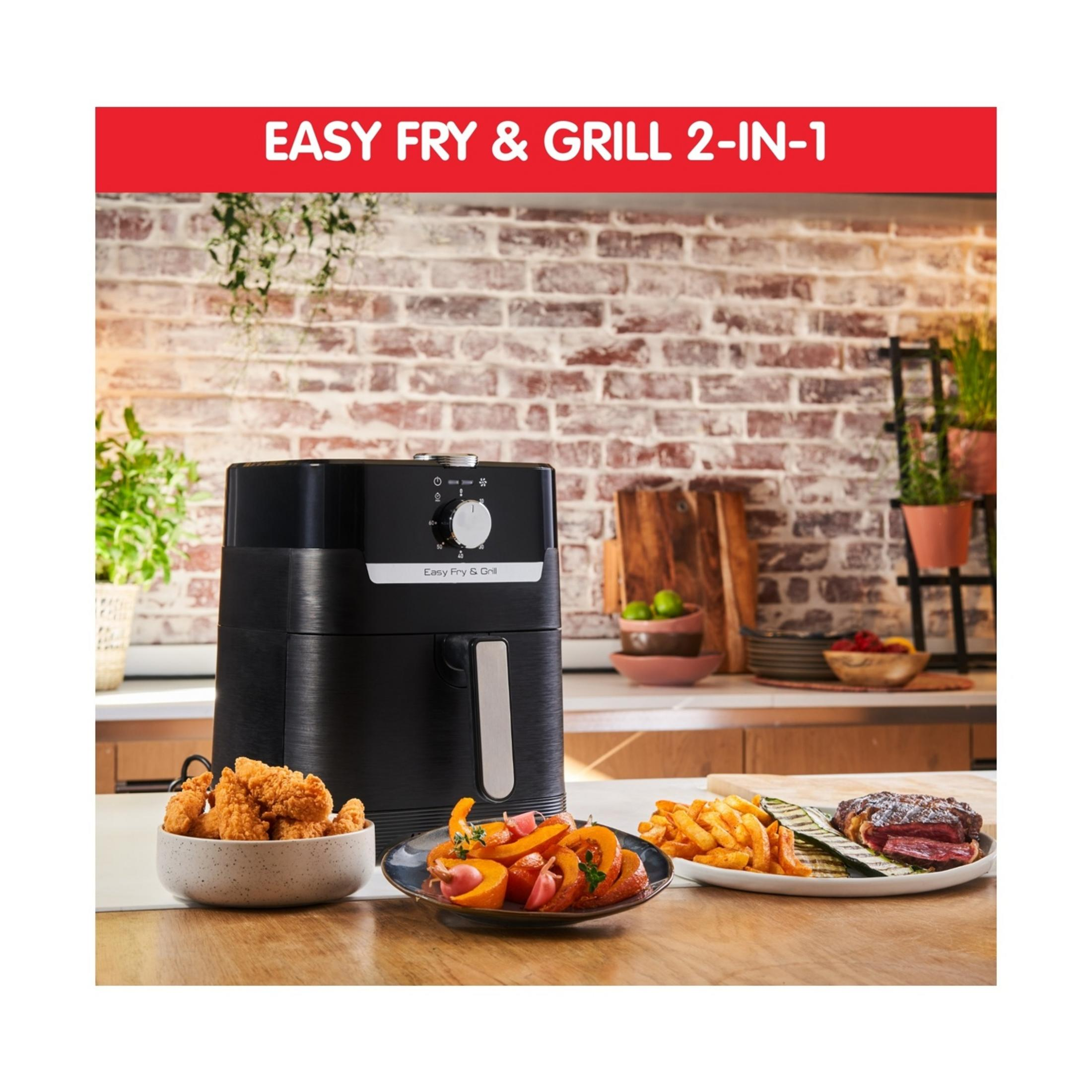 Czarna frytkownica beztłuszczowa z kurczakiem, warzywami i stekiem na stole.