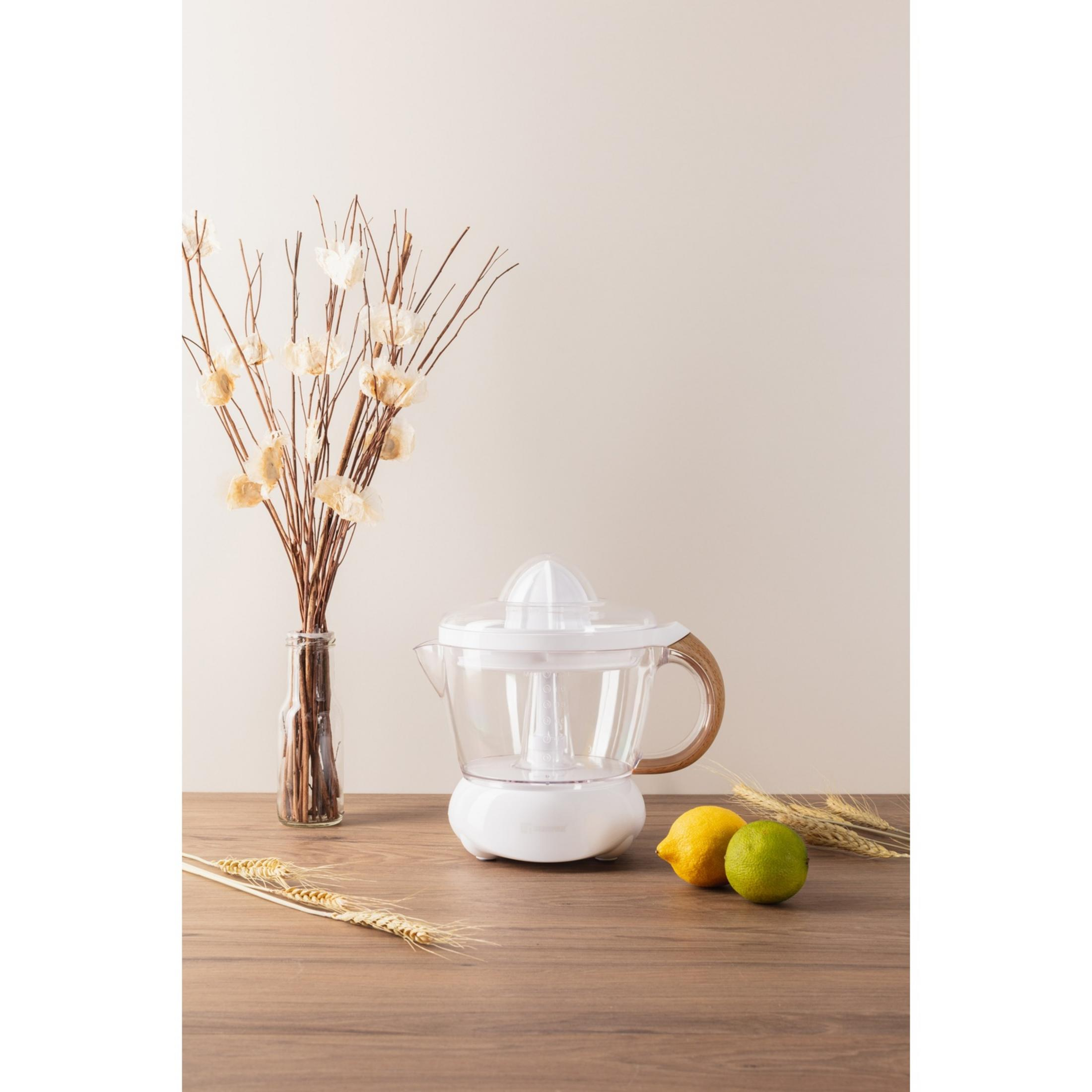 Un exprimidor blanco con mango de madera sobre mesa de madera, junto a cítricos y flores secas.