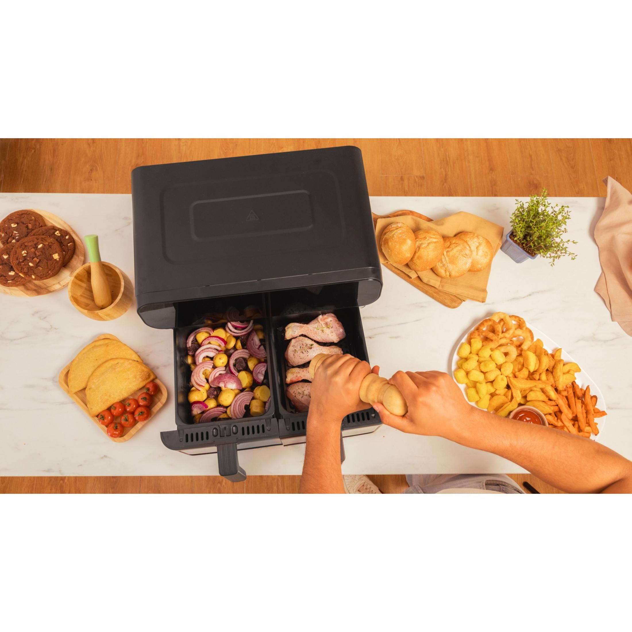 Een dubbele airfryer met kippendijen en aardappelen. Bijgerechten zijn broodjes, koekjes, taco's en friet.