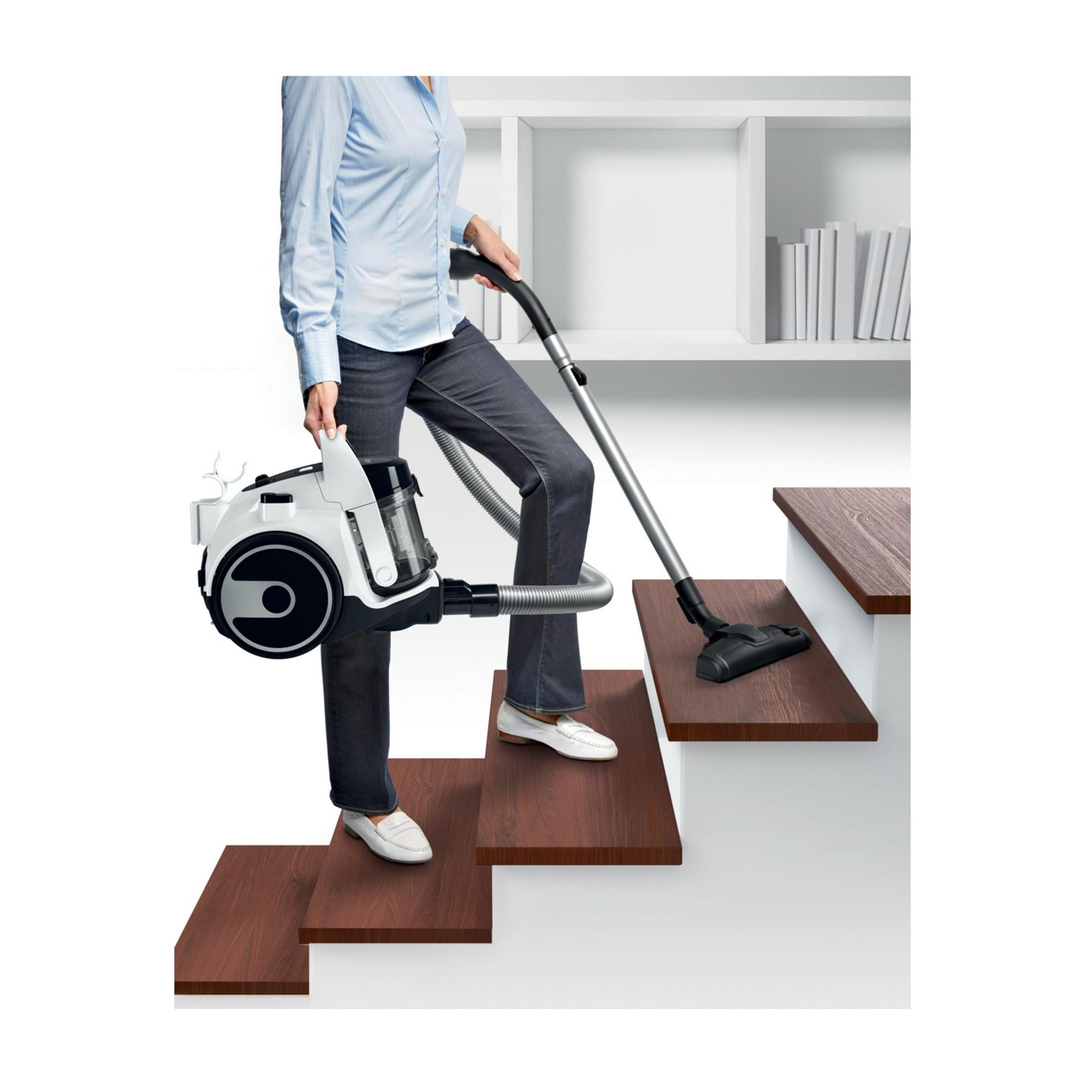 Osoba odkurza drewniane schody białym odkurzaczem.