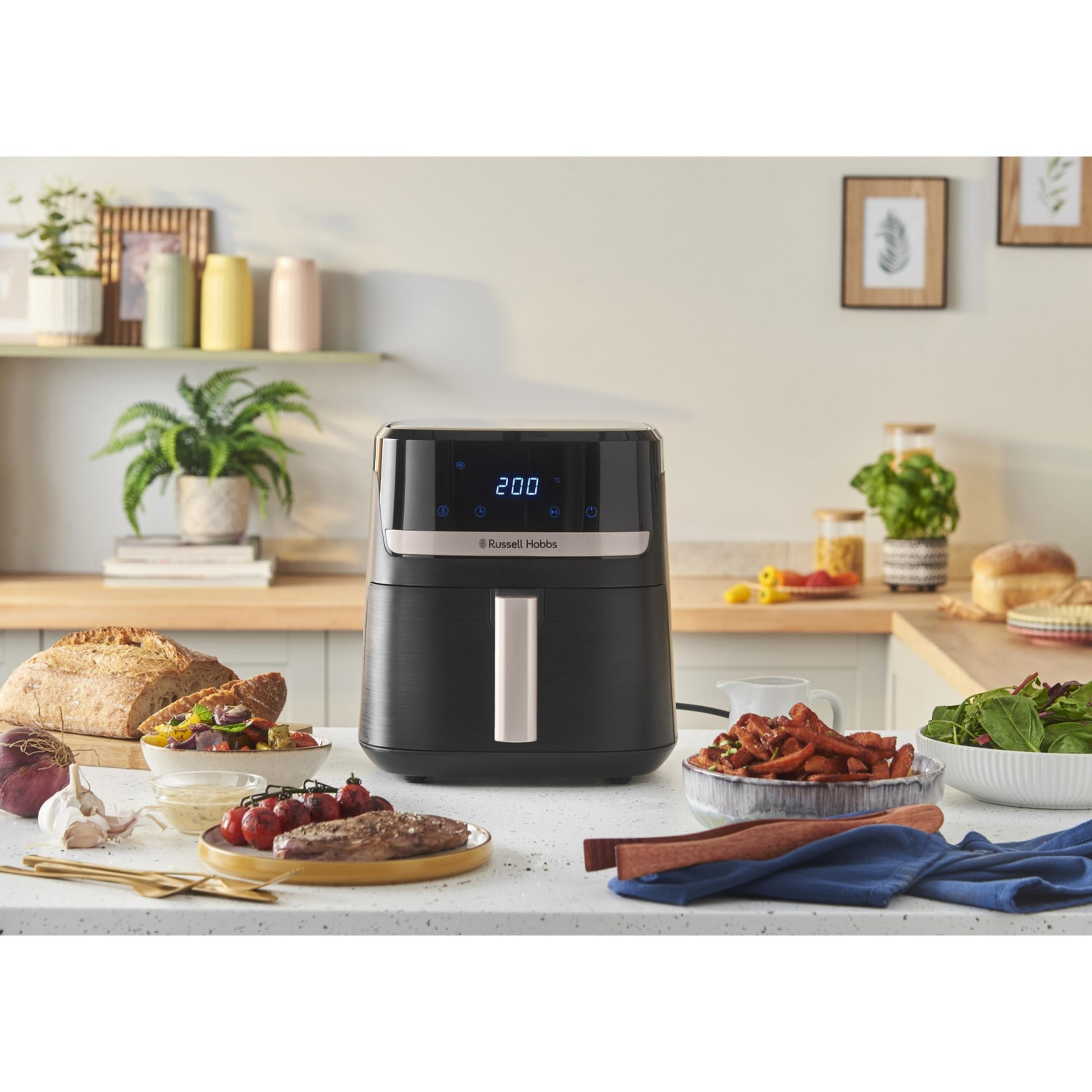 Una freidora de aire Russell Hobbs negra en una encimera con comida alrededor.