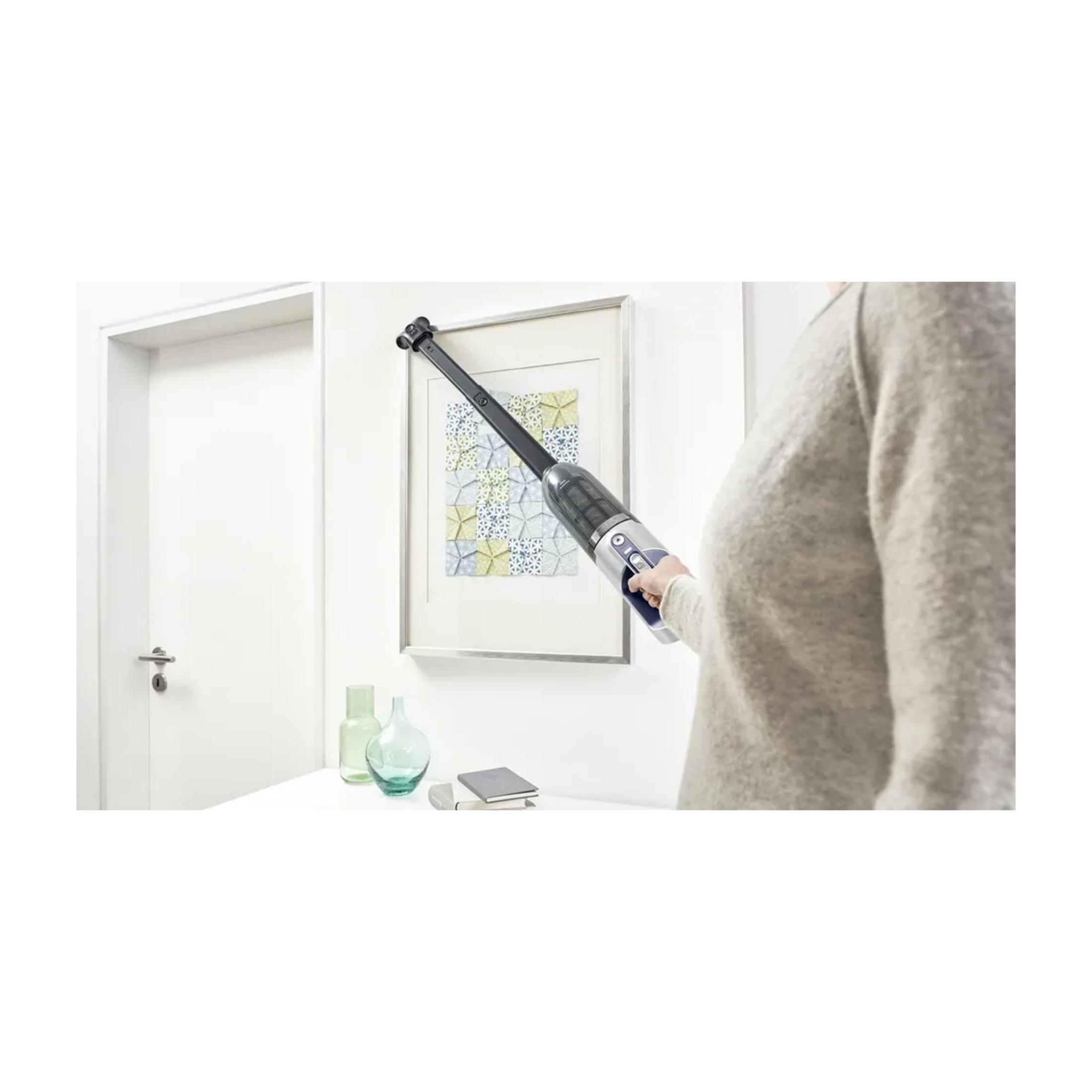 Una persona limpia un cuadro en la pared con una aspiradora de mano.