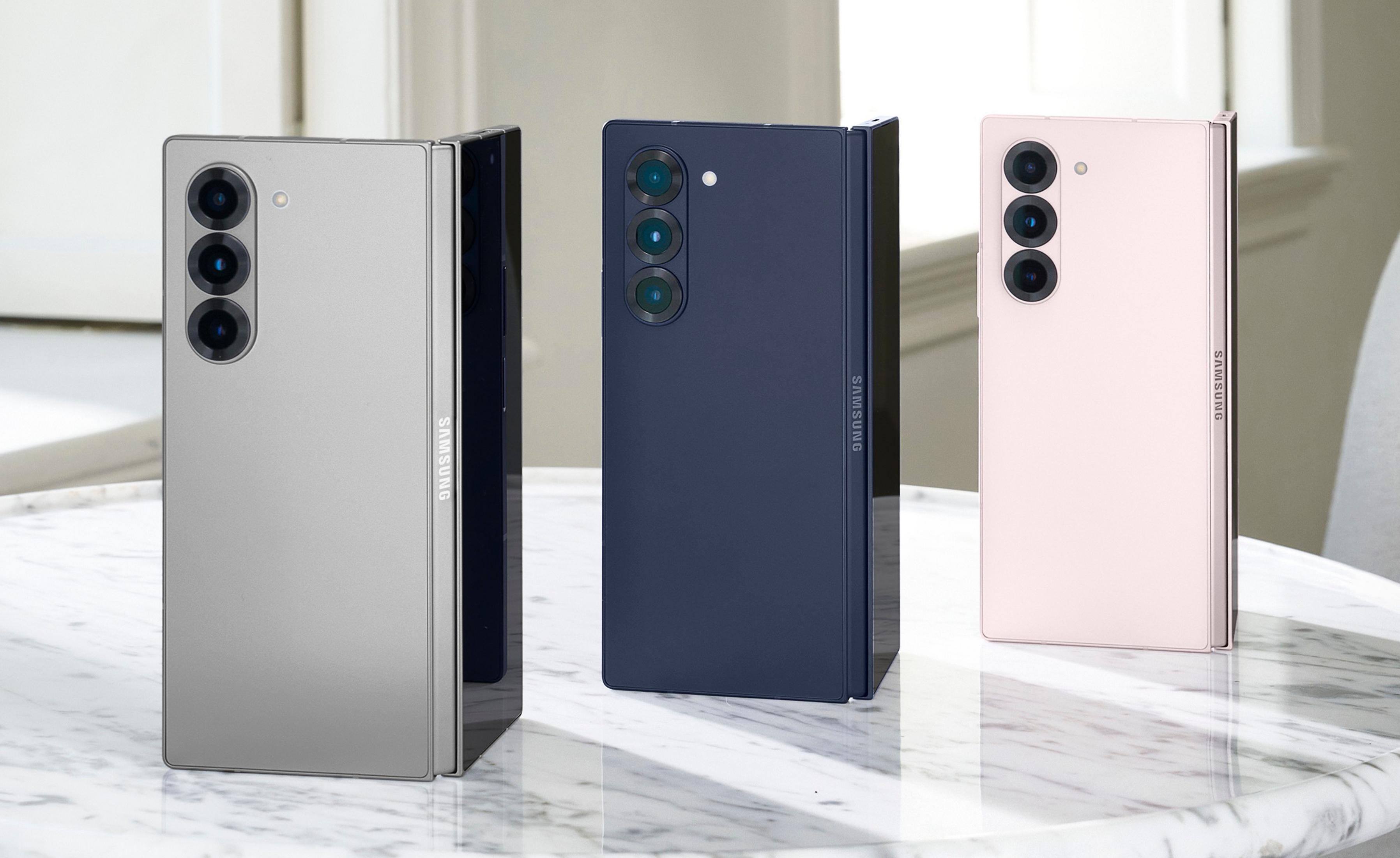 Drei Samsung Fold-Smartphones in Silber, Dunkelblau und Rosa auf einem Marmortisch.