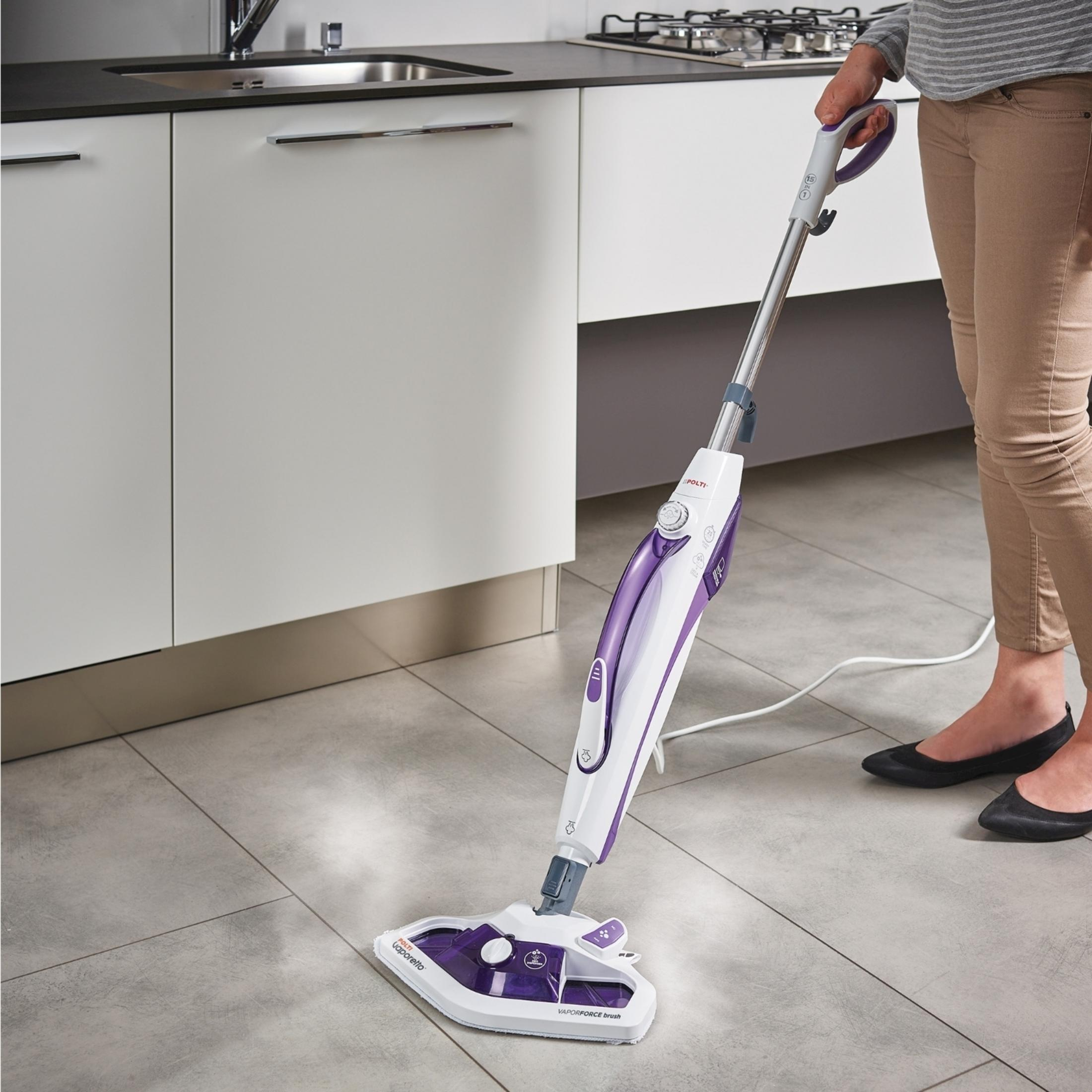 Osoba czyści szarą podłogę z płytek fioletowo-białą mopem parowym.
