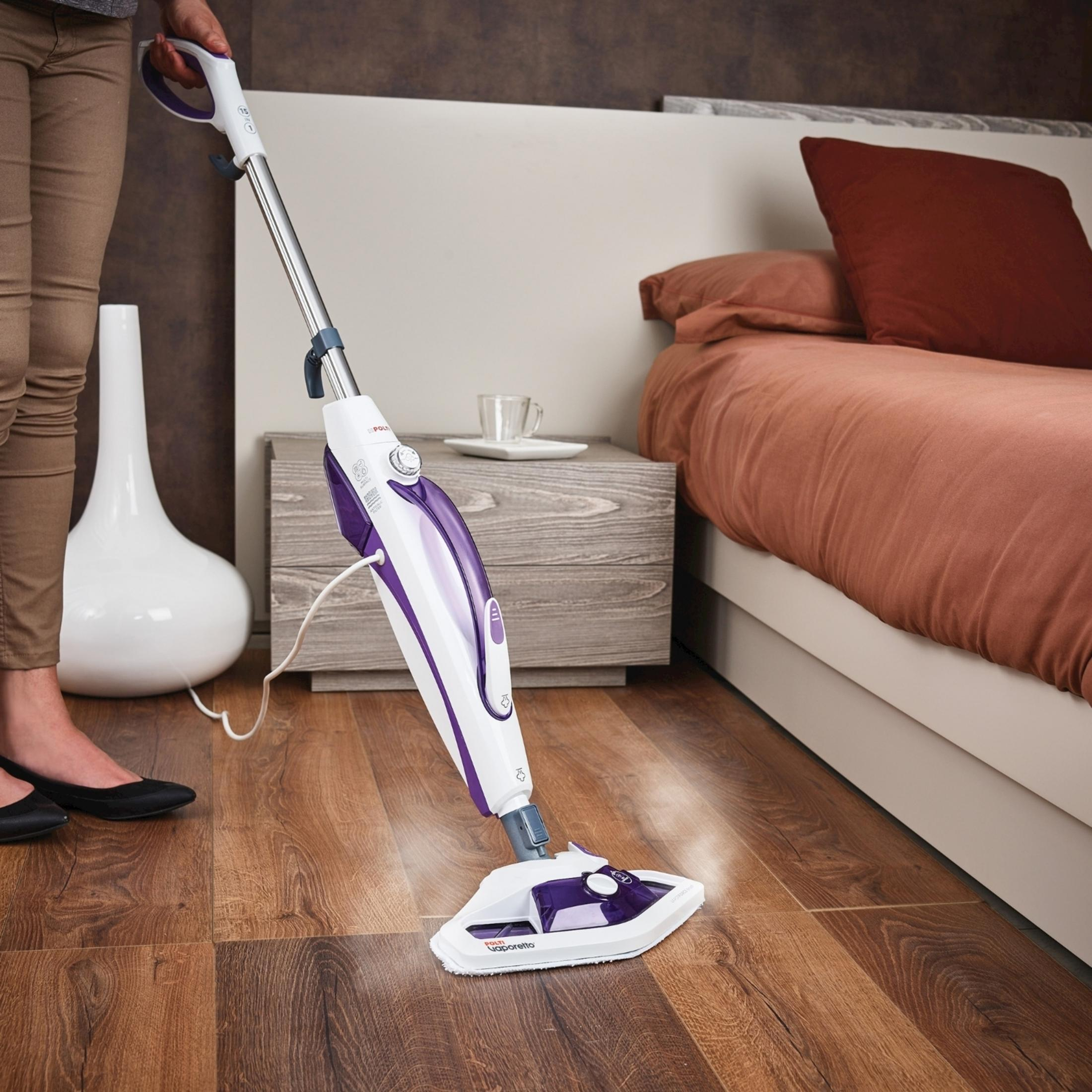 Osoba czyści drewnianą podłogę mopem parowym obok łóżka.