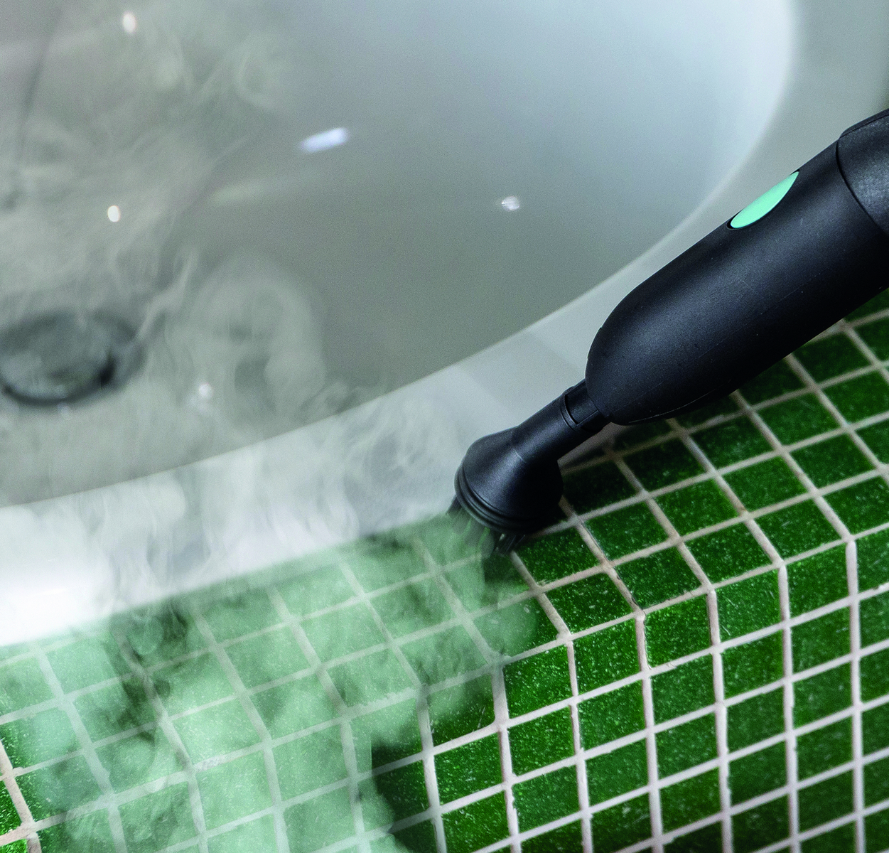 Eine schwarze Dampfreinigungsdüse sprüht Dampf auf grüne Fliesenfugen neben einer weißen Badewanne.