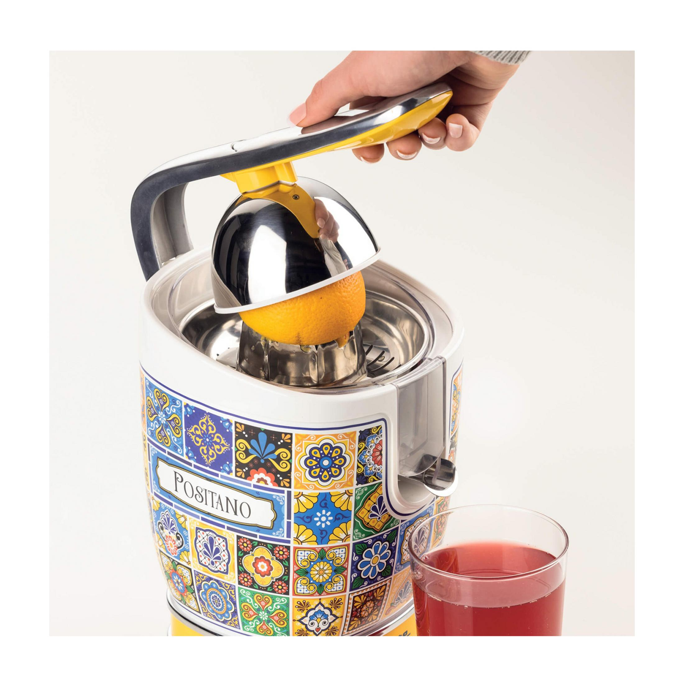 Eine Hand drückt eine Orange auf einen dekorativen Entsafter neben einem Glas Saft.