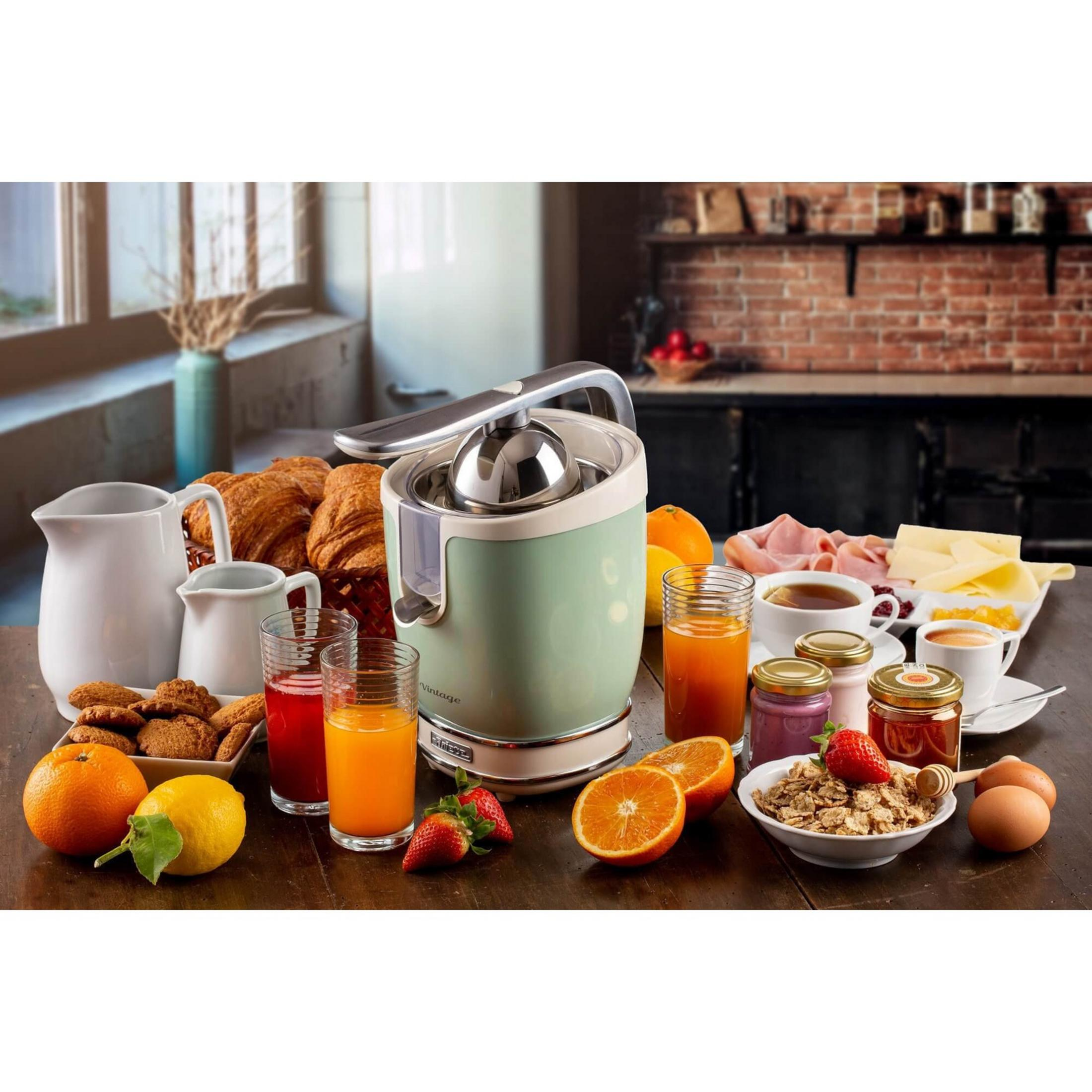 Stół śniadaniowy z wyciskarką, rogalikami, owocami, płatkami i kawą.