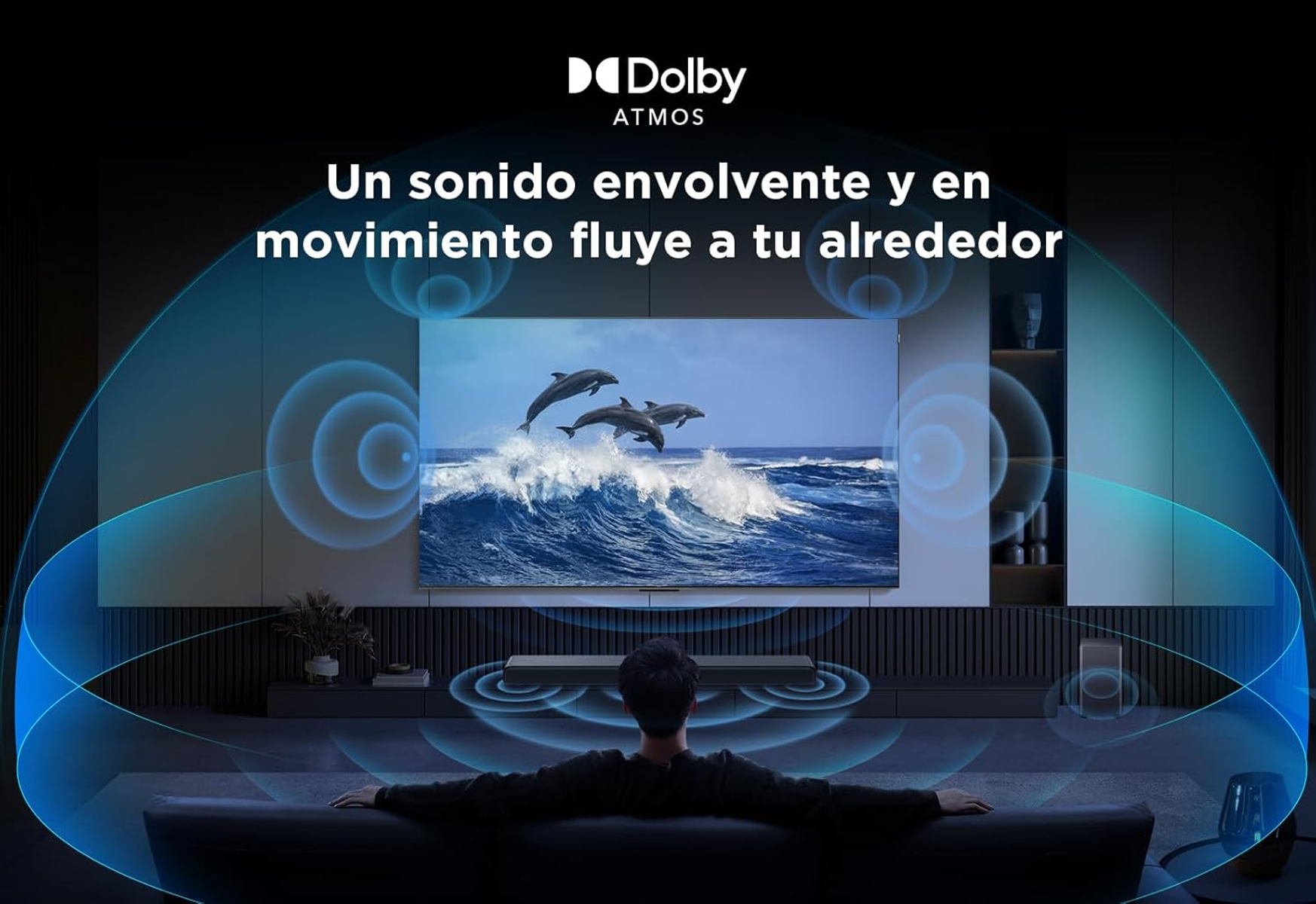 Mężczyzna na kanapie ogląda TV z wyskakującymi delfinami. Logo Dolby Atmos.