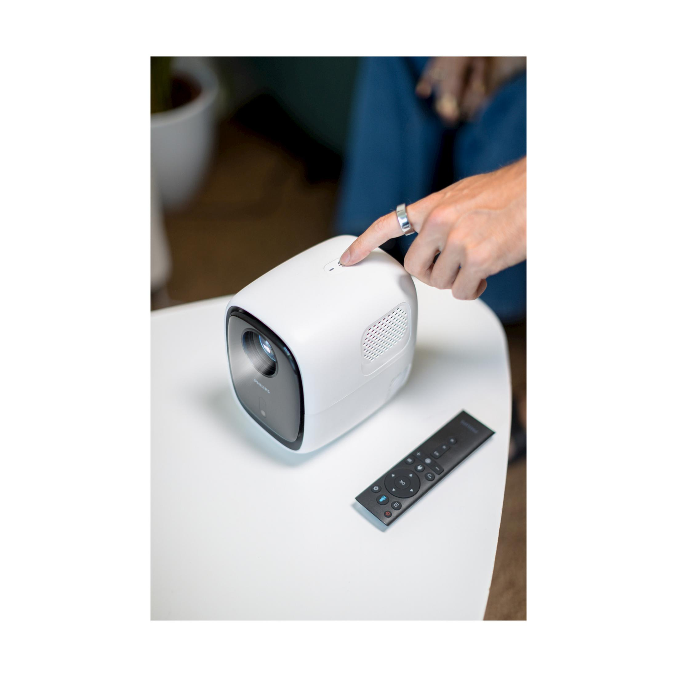 Beyaz bir Philips projektör ve bir uzaktan kumanda masanın üzerinde.