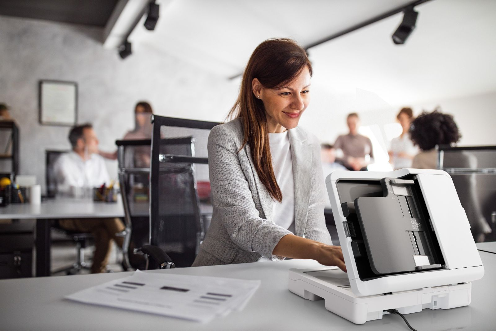 Een vrouw in een kantoor gebruikt een scanner, met collega's op de achtergrond.
