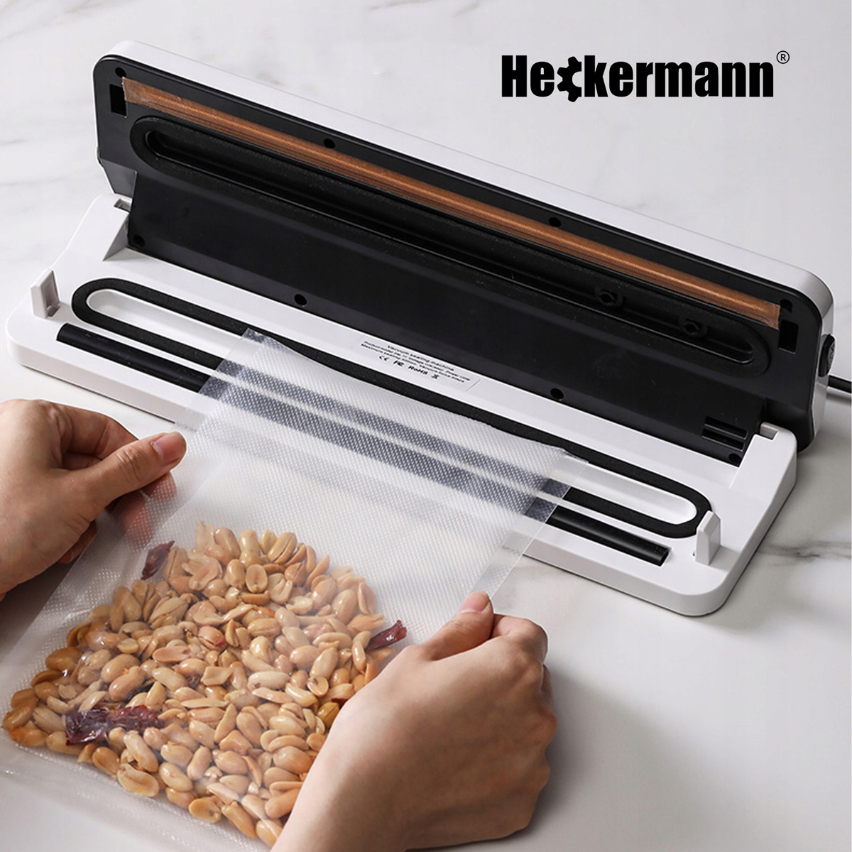 Ręce wkładają worek z orzeszkami ziemnymi do białej zgrzewarki próżniowej.