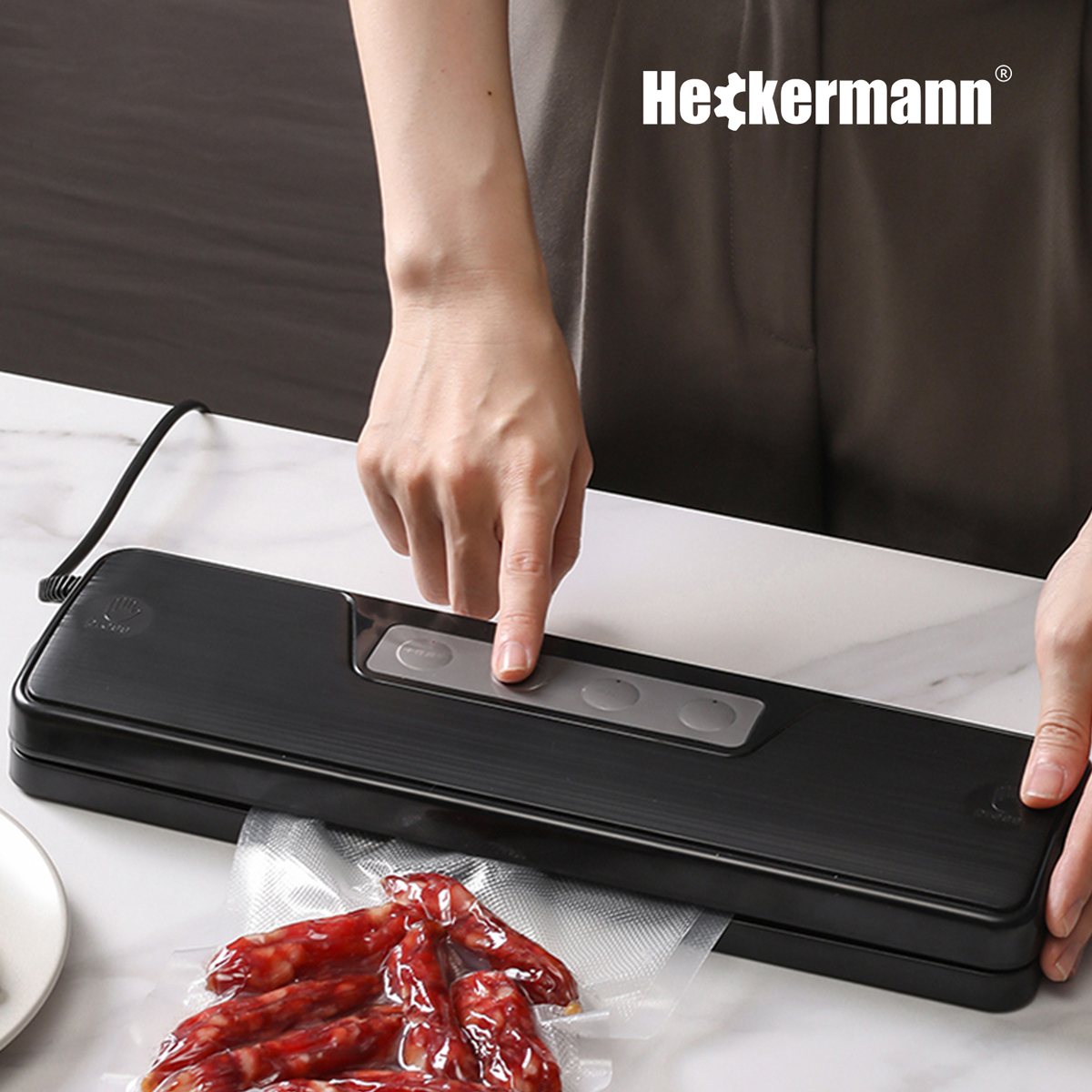 Osoba obsługuje czarną zgrzewarkę próżniową z kiełbasą w worku.