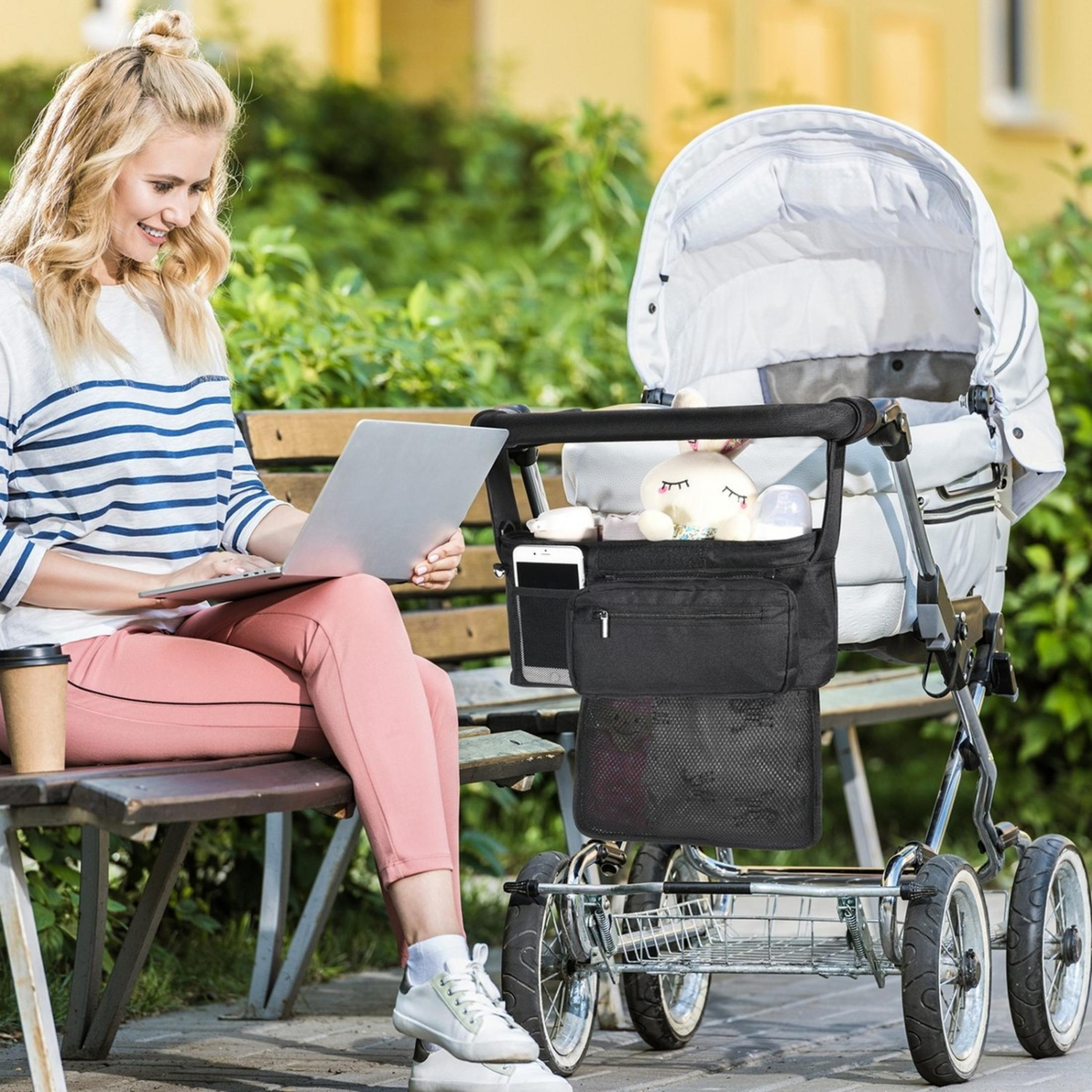 Una donna seduta su una panchina lavora al laptop accanto a un passeggino.