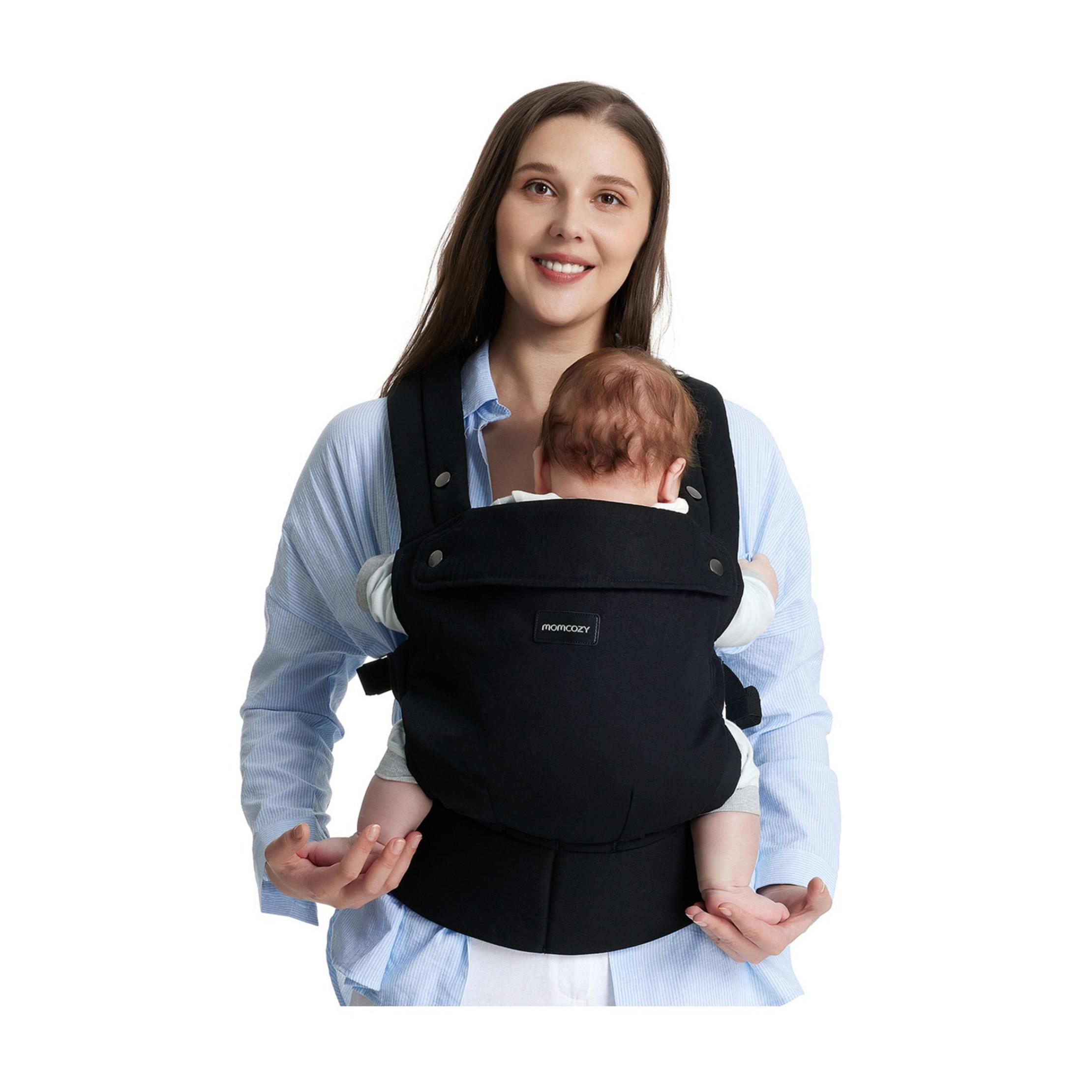 A woman wearing a blue striped shirt holds a baby in a black carrier.