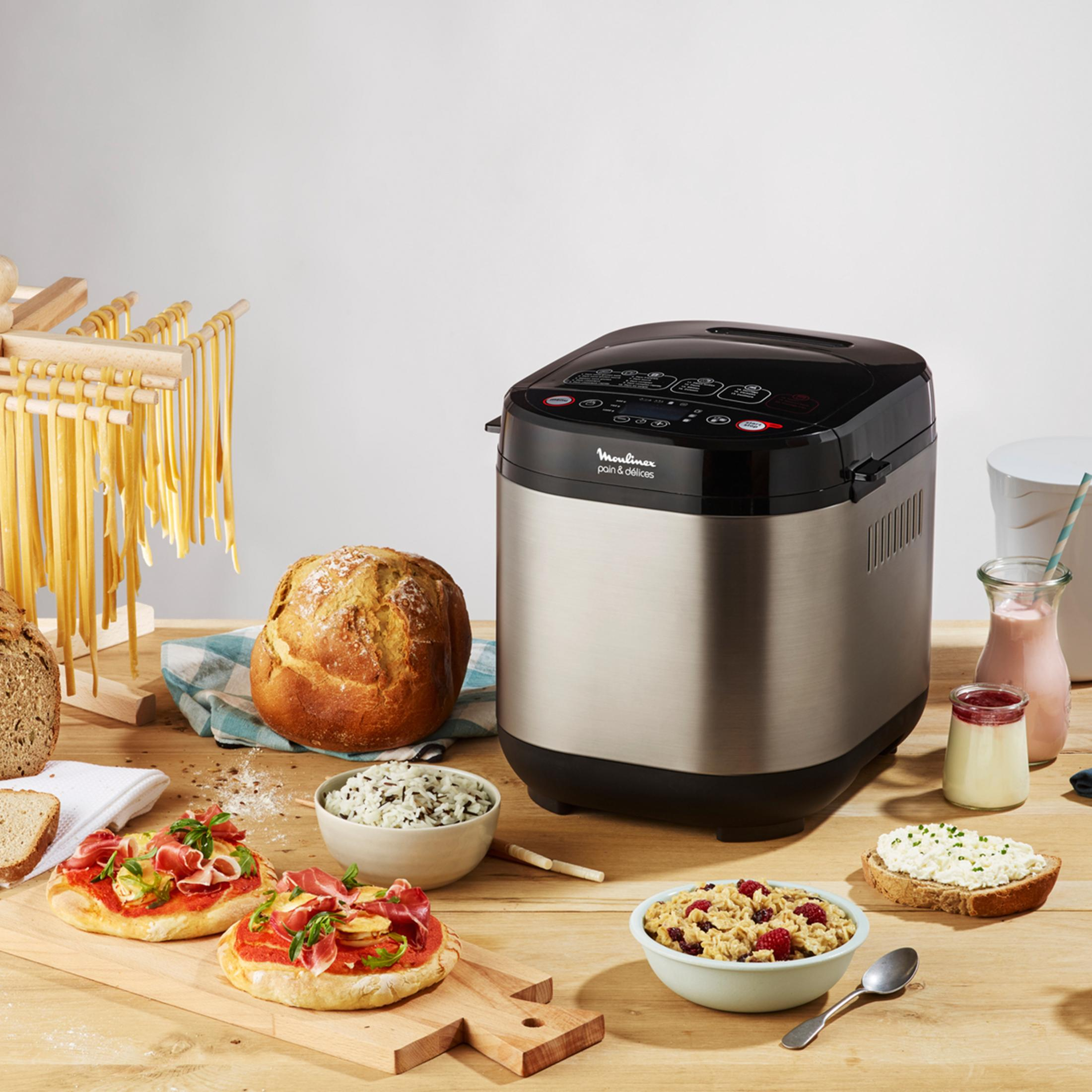 Brotbackautomat mit Brot, Nudeln, Snacks und Desserts auf Holztisch.