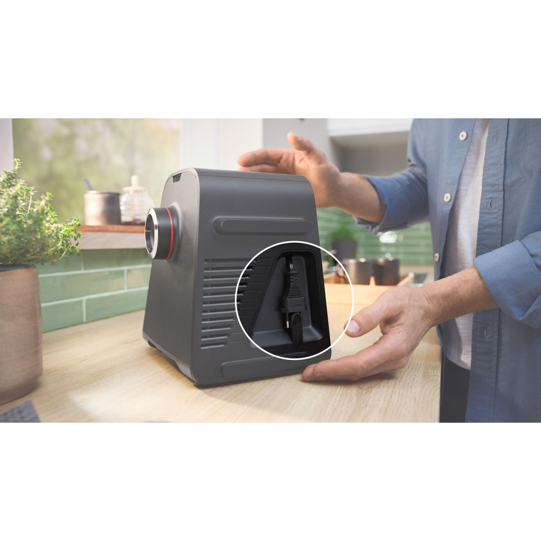 Mężczyzna podłącza czarny kabel zasilający do szarego urządzenia na drewnianym blacie.