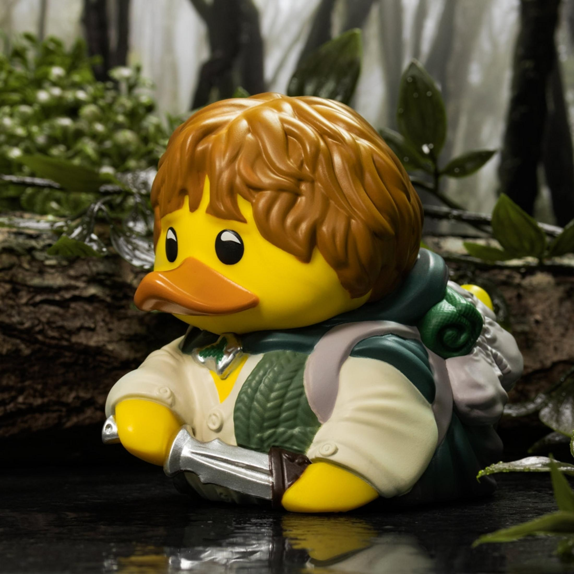 Gelbe Gummi-Ente mit braunem Haar, Schwert, Rucksack im Wald.