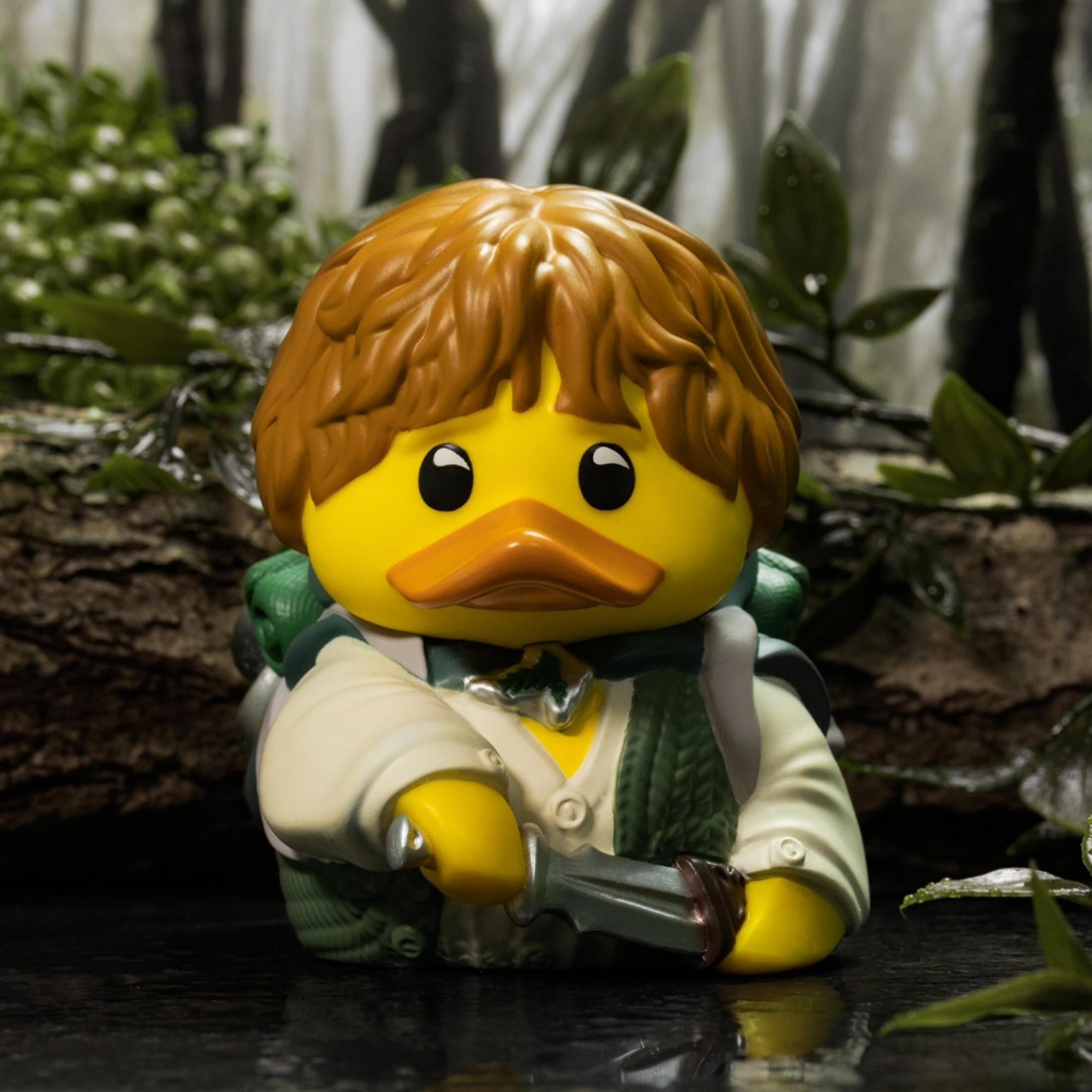 Eine gelbe Gummiente mit braunem Haar, die ein Messer hält, im Wald.