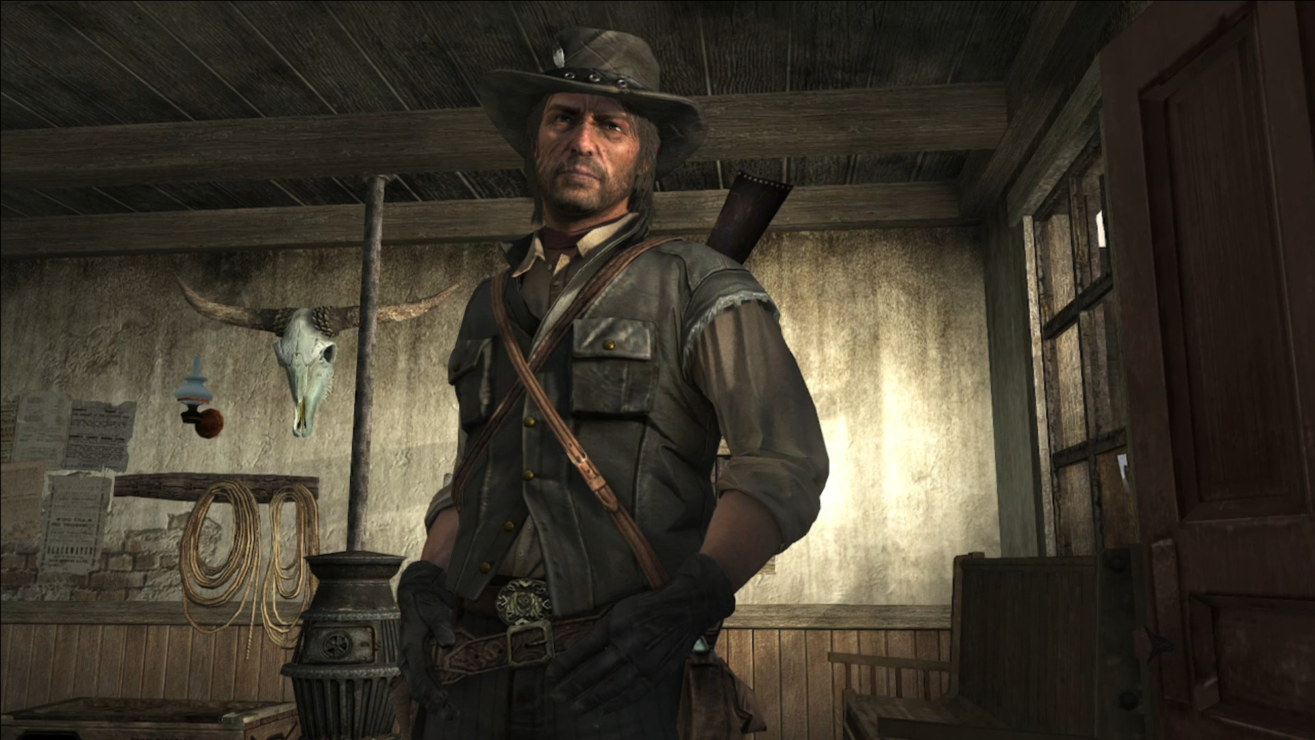 Un uomo con cappello da cowboy si trova in una stanza con un teschio di toro sul muro.