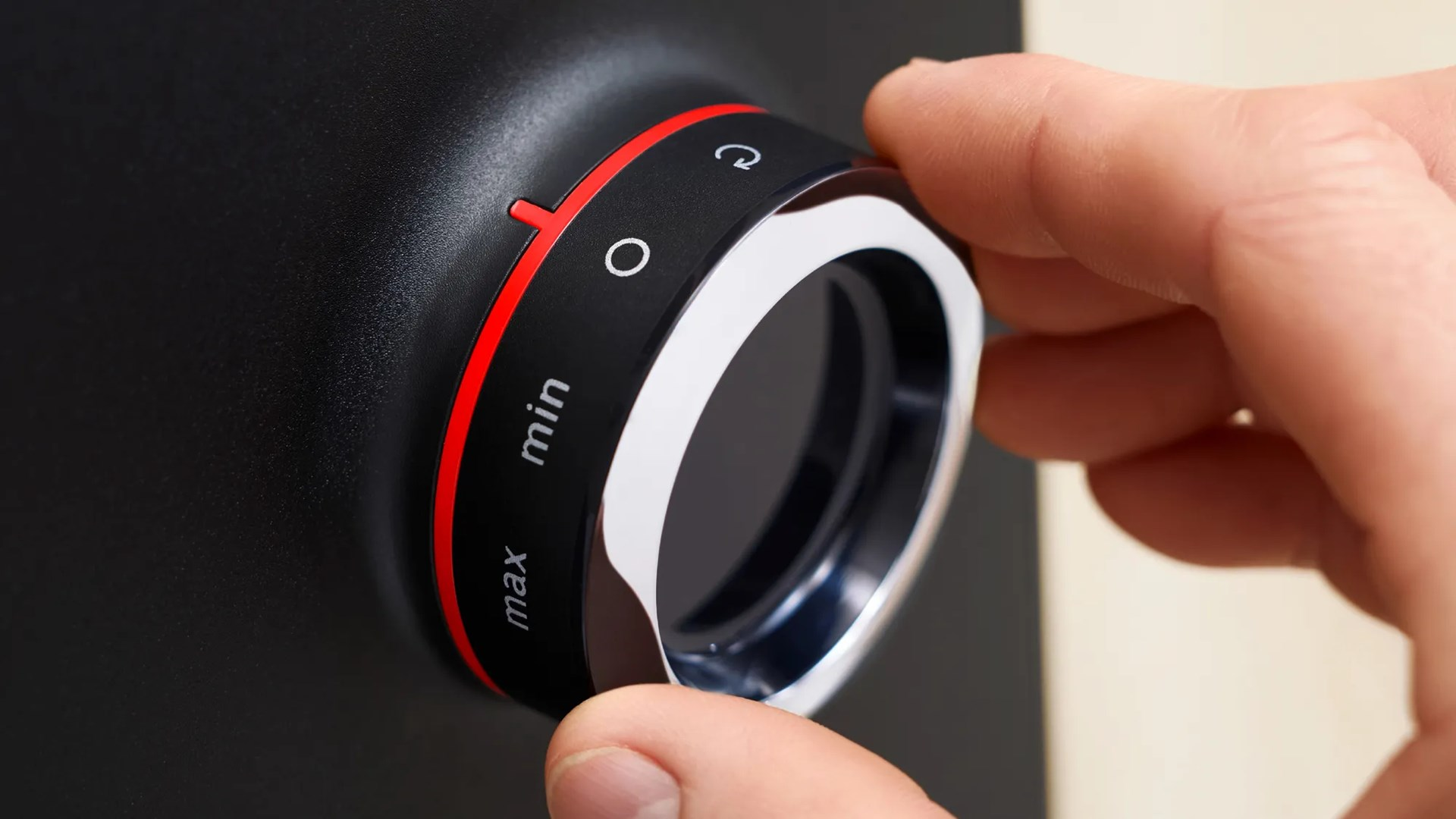 Dłoń obraca czarne pokrętło z czerwonymi i białymi oznaczeniami.