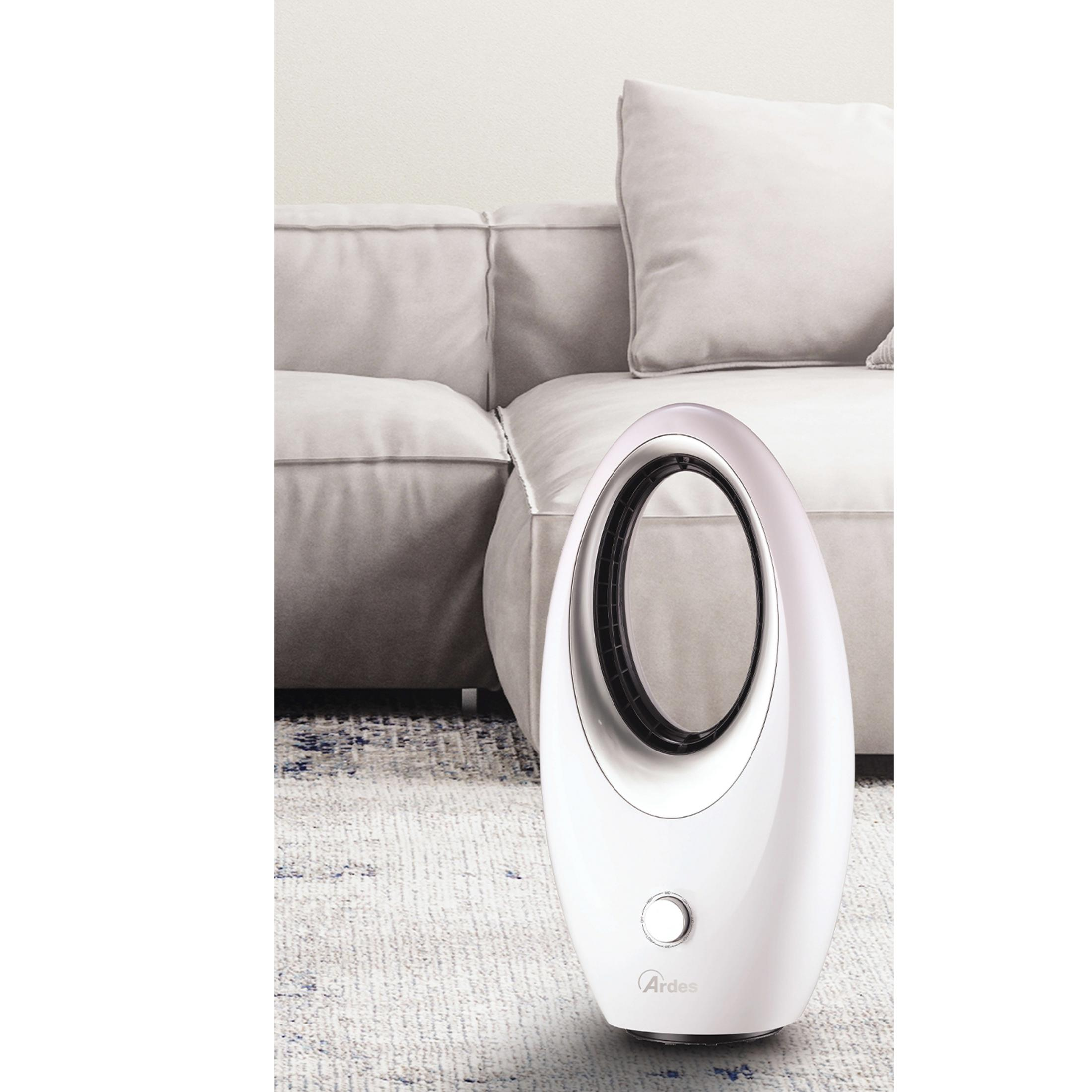 Biały wentylator stoi na dywanie przed sofą.