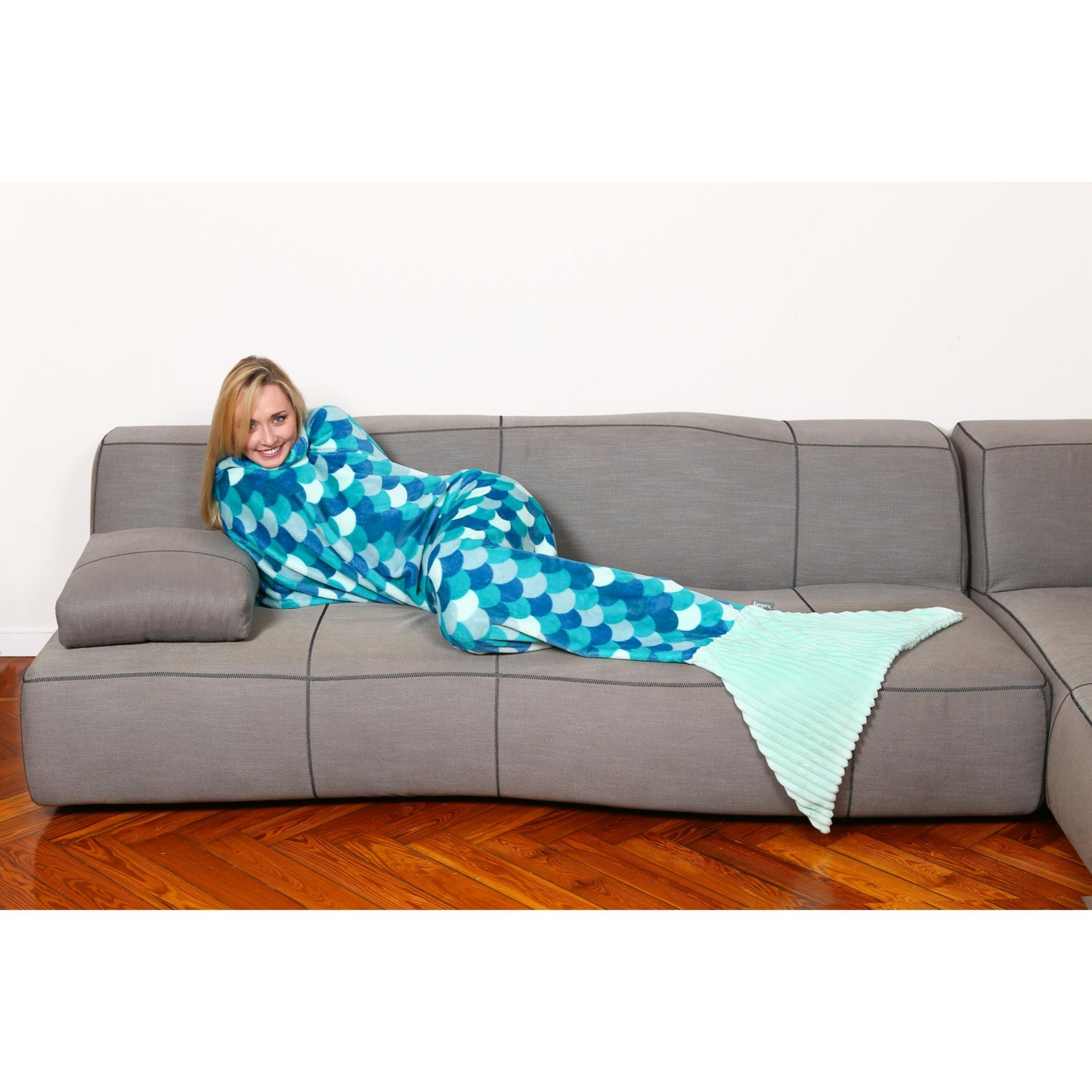Donna in un sacco a pelo da sirena blu giace su un divano grigio.