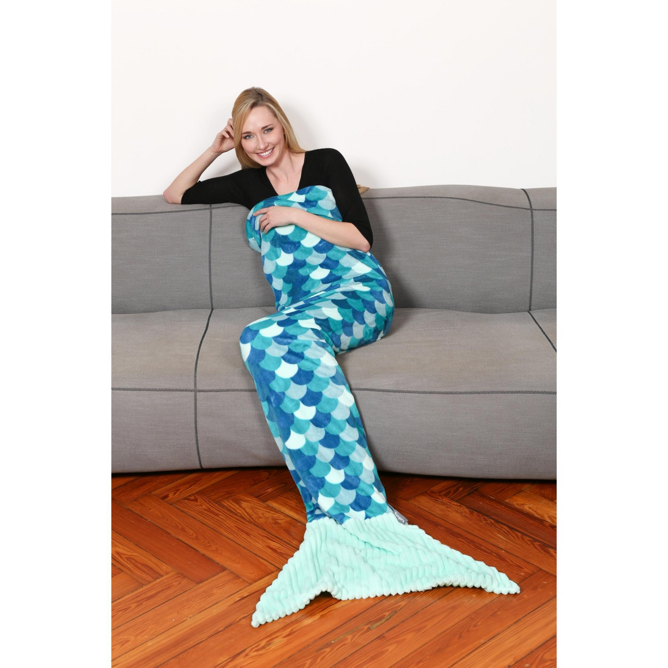 Una donna seduta su un divano che tiene una coperta a coda di sirena blu e verde.