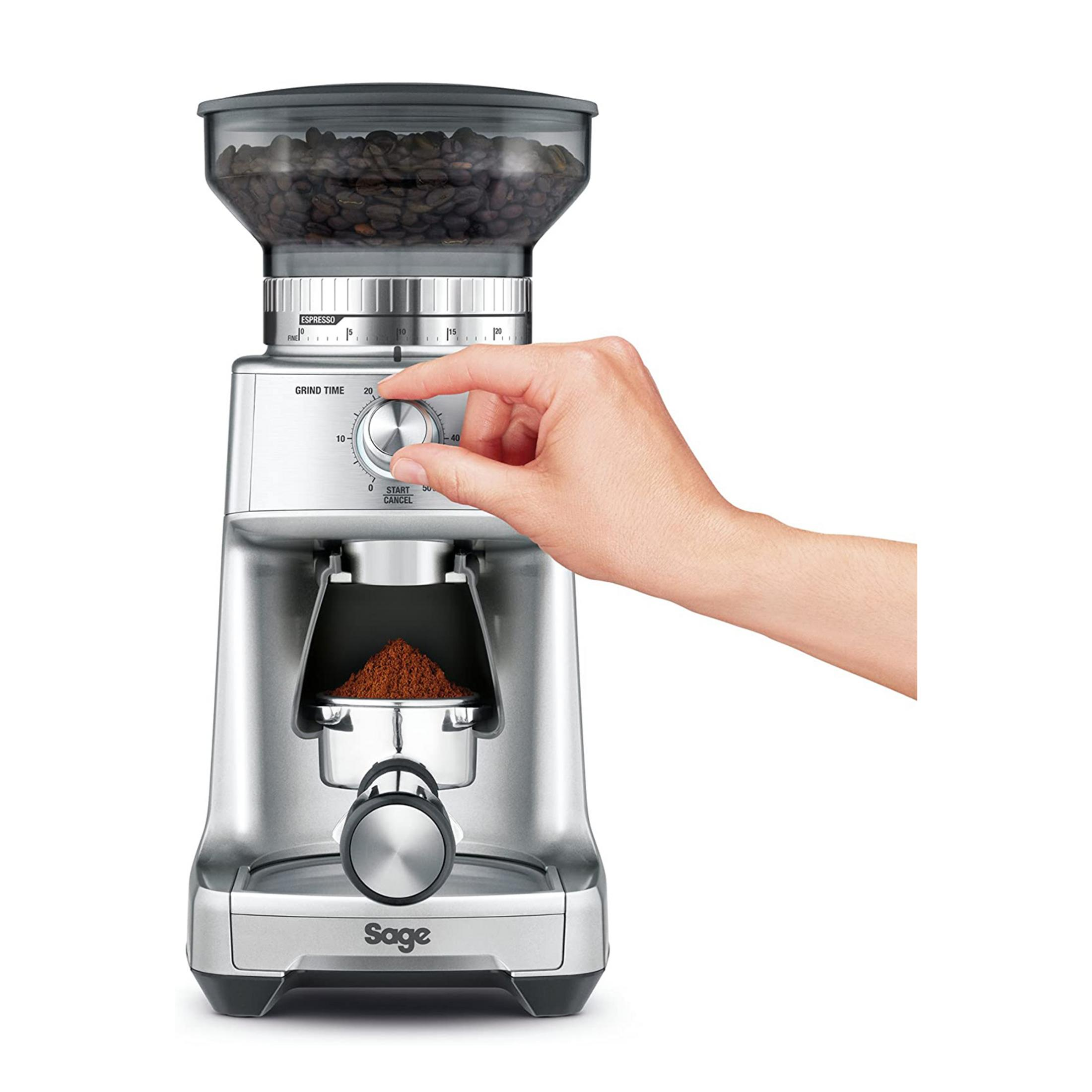 Una mano gira un dial en un molinillo de café plateado con granos de café.