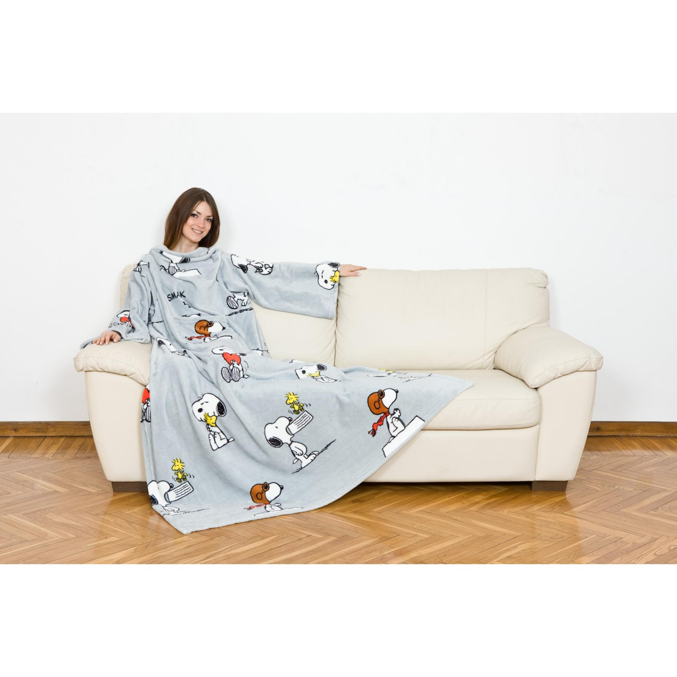 Una donna seduta su un divano, avvolta in una coperta grigia con personaggi di Snoopy.