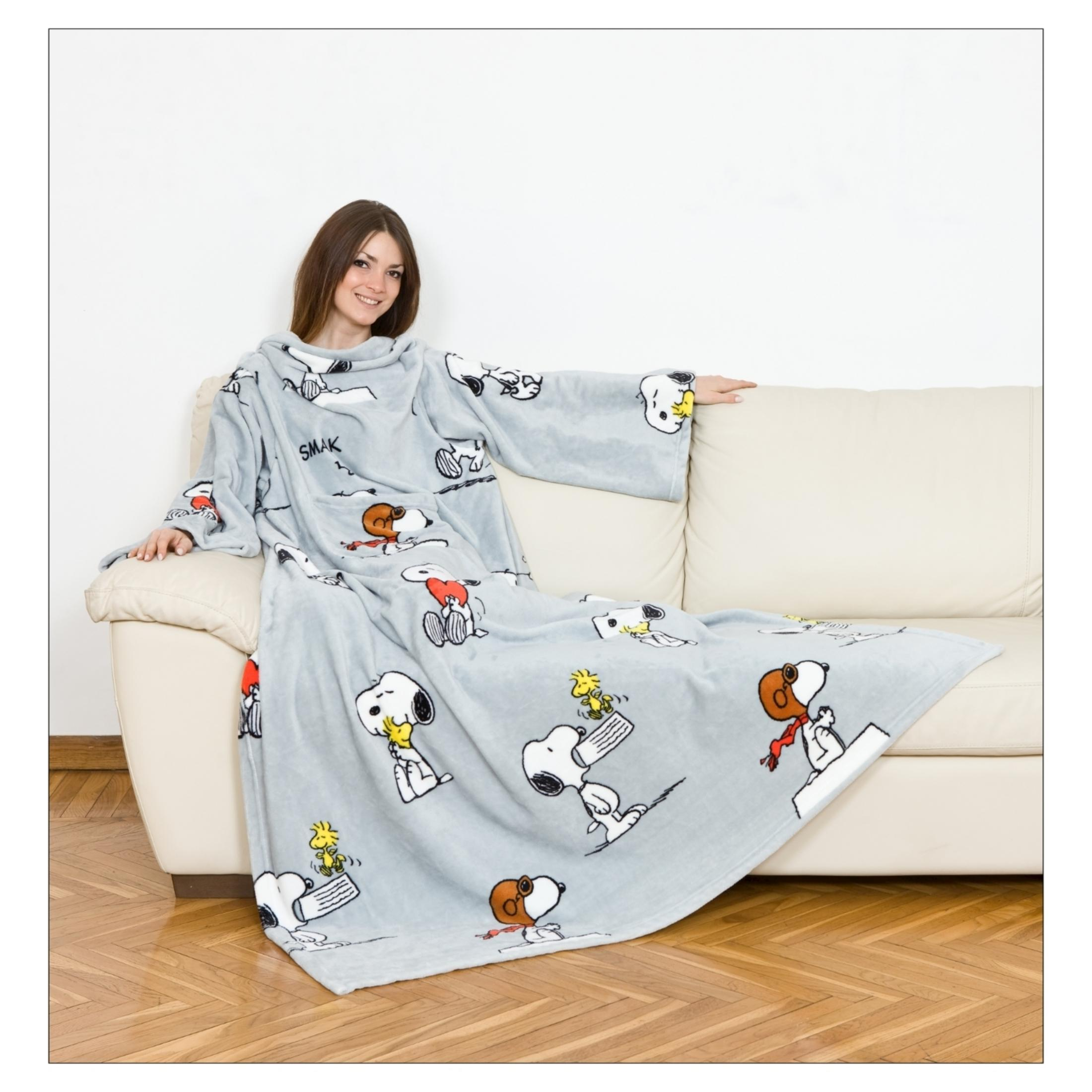 Una donna seduta su un divano indossa una coperta indossabile grigia con Snoopy.