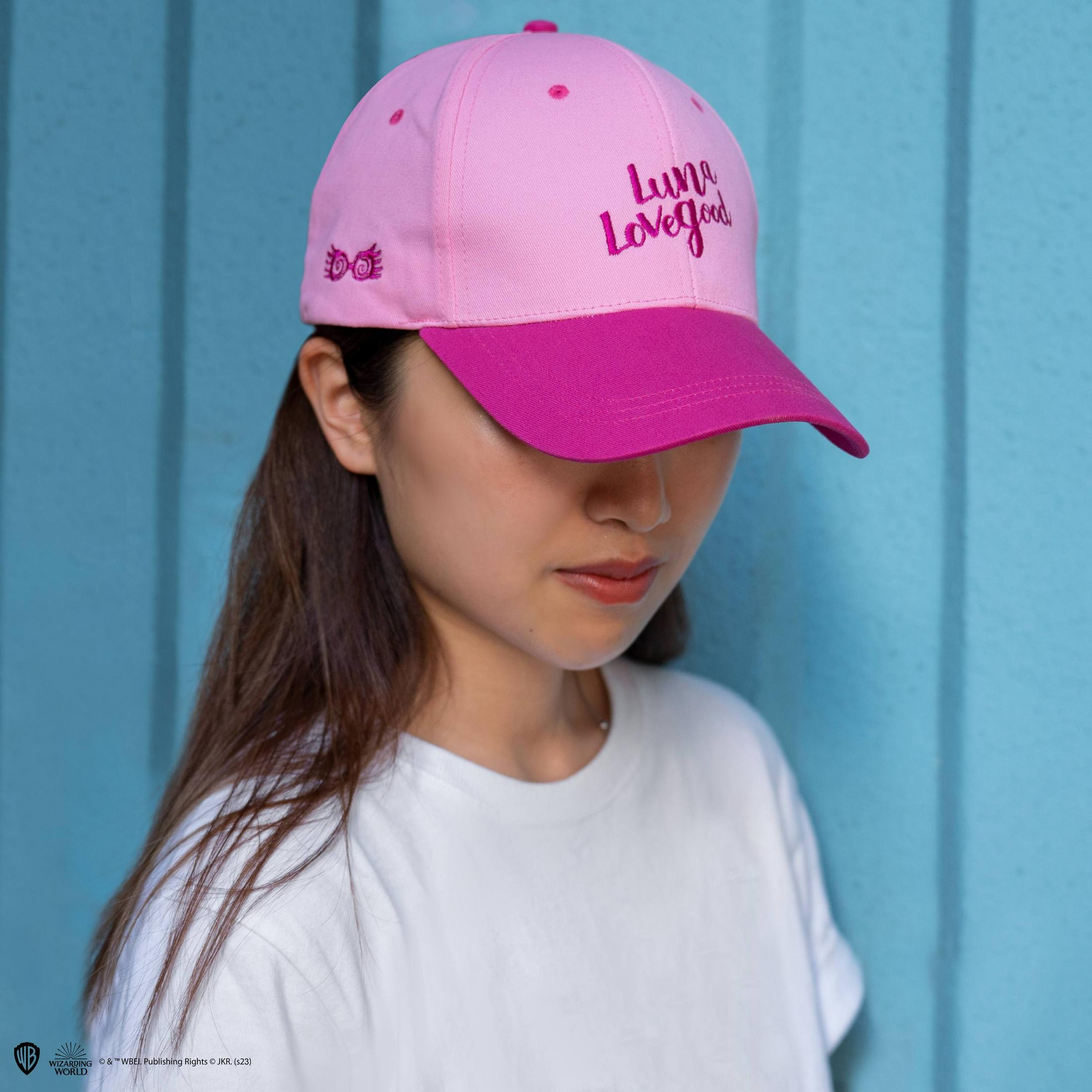 Una mujer lleva una gorra rosa con el texto 'Luna Lovegood' y un emblema.