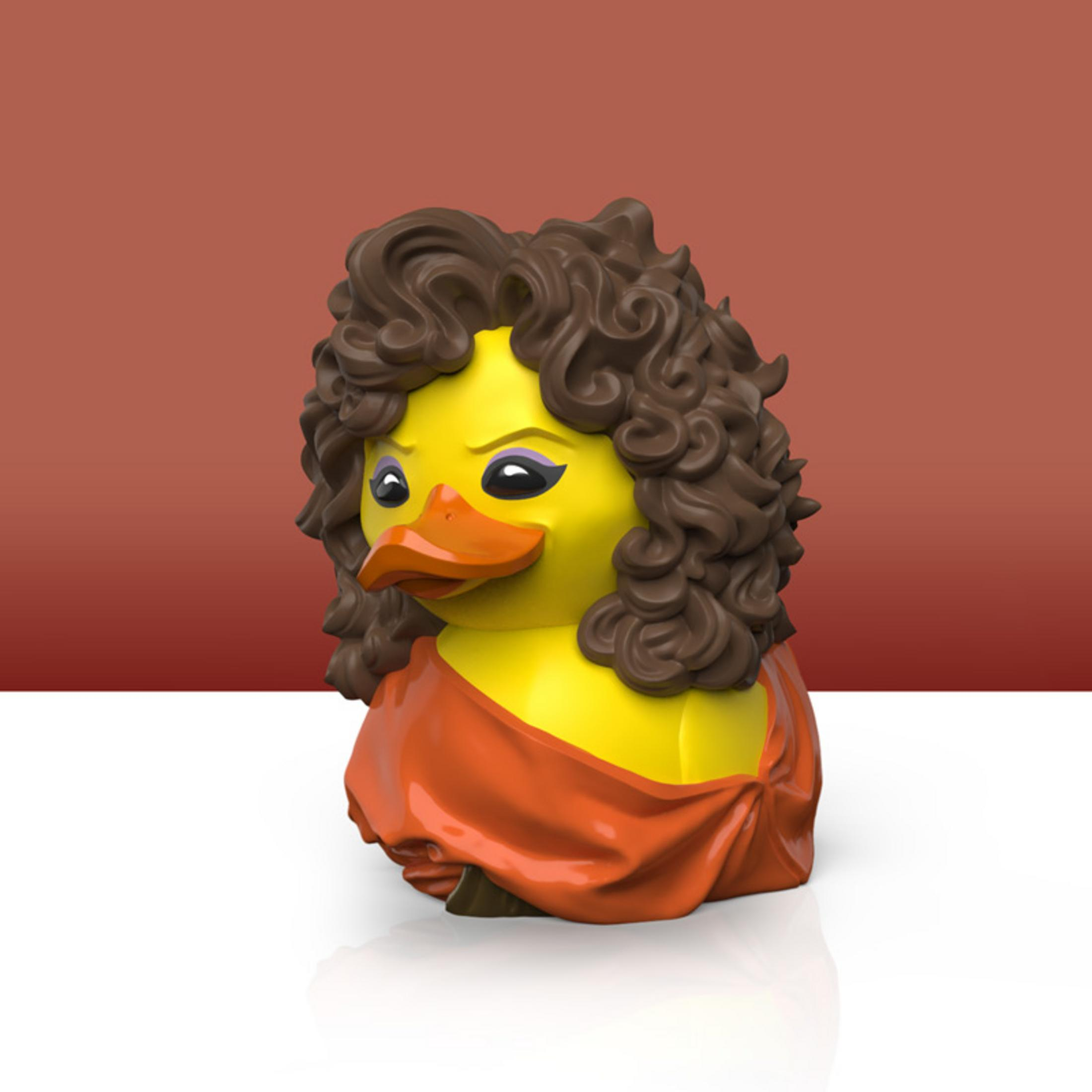 Eine gelbe Gummi-Ente mit braunen Locken und einem orangefarbenen Kleid.