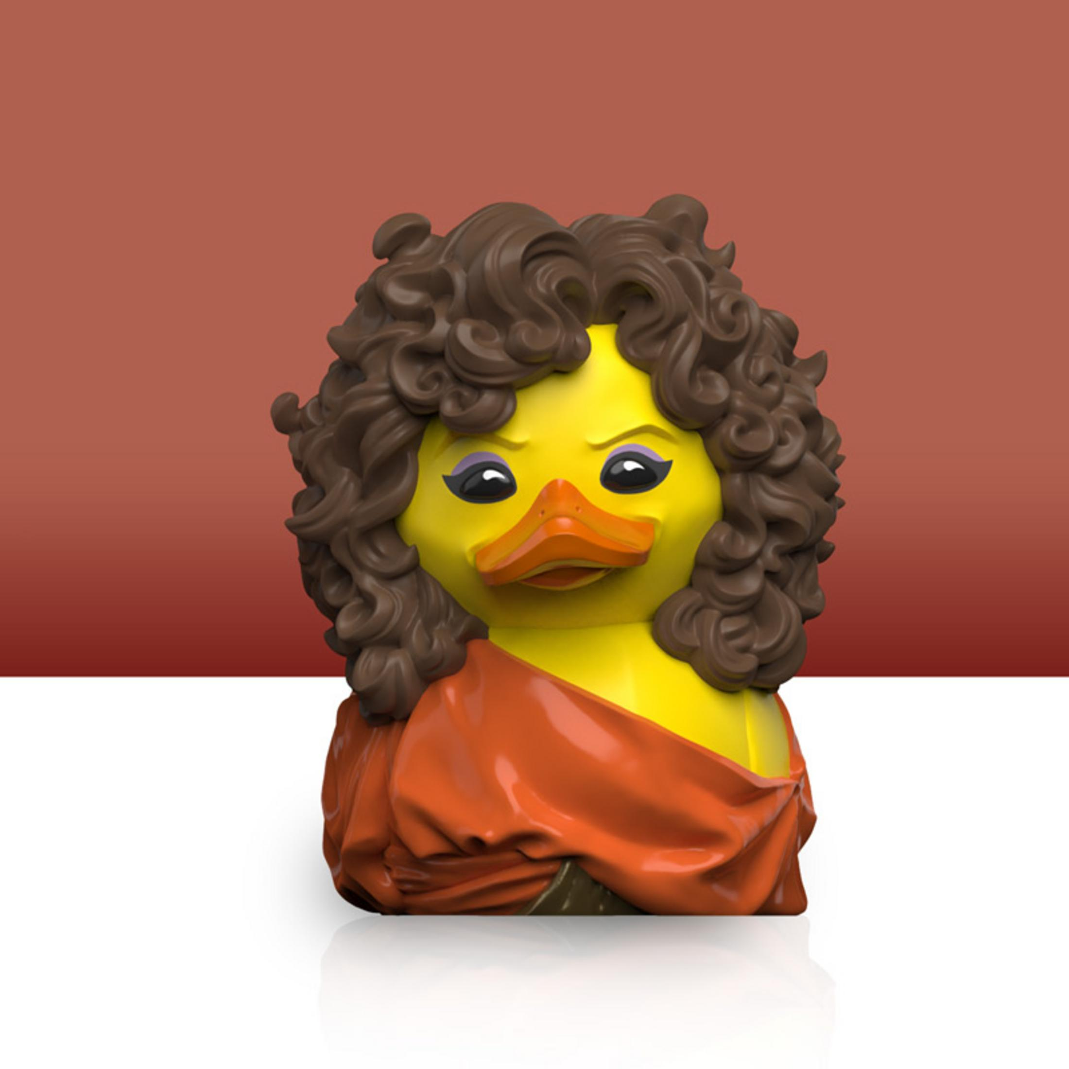 Eine gelbe Gummi-Ente mit brauner Lockenperücke und orangefarbenem Umhang.