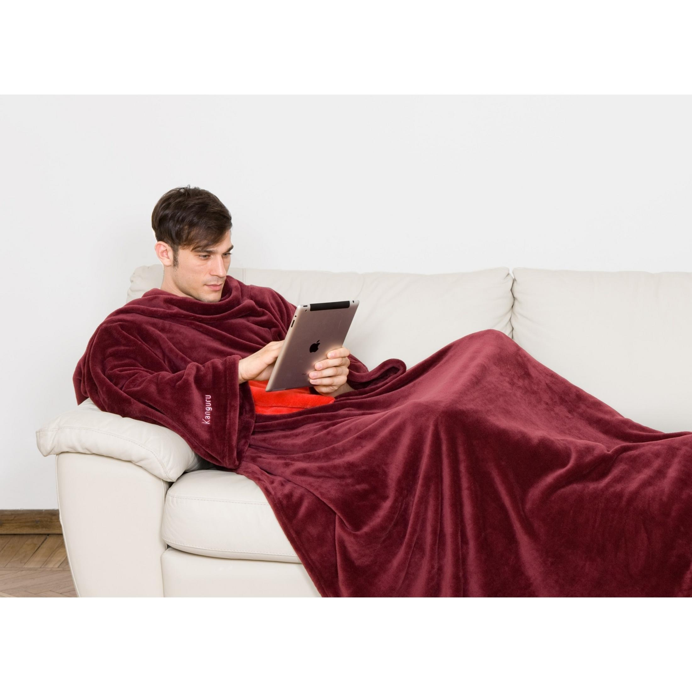 Uomo con tablet sul divano, avvolto in coperta color vinaccia.