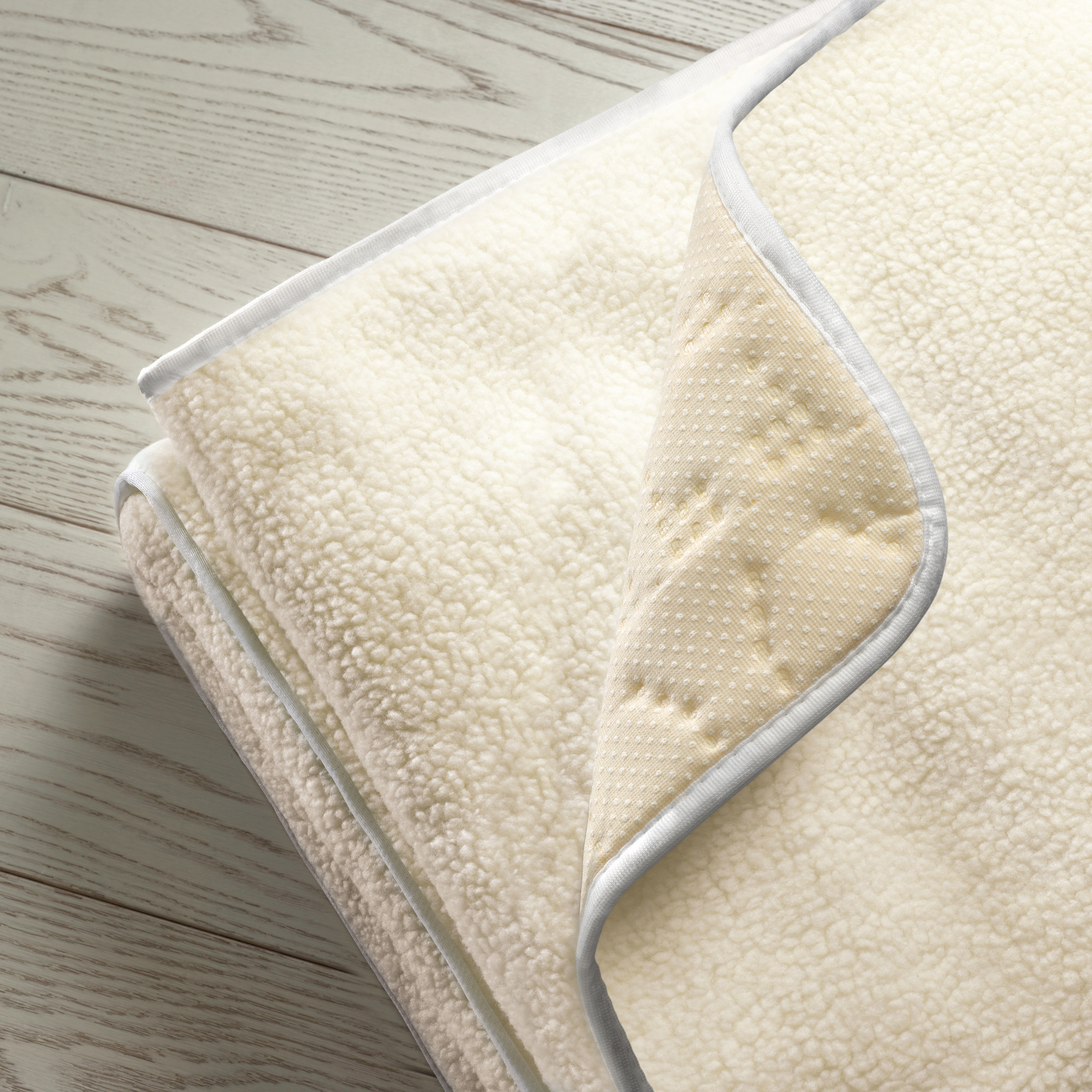 Una alfombra suave de piel de oveja color crema con reverso antideslizante sobre suelo de madera.