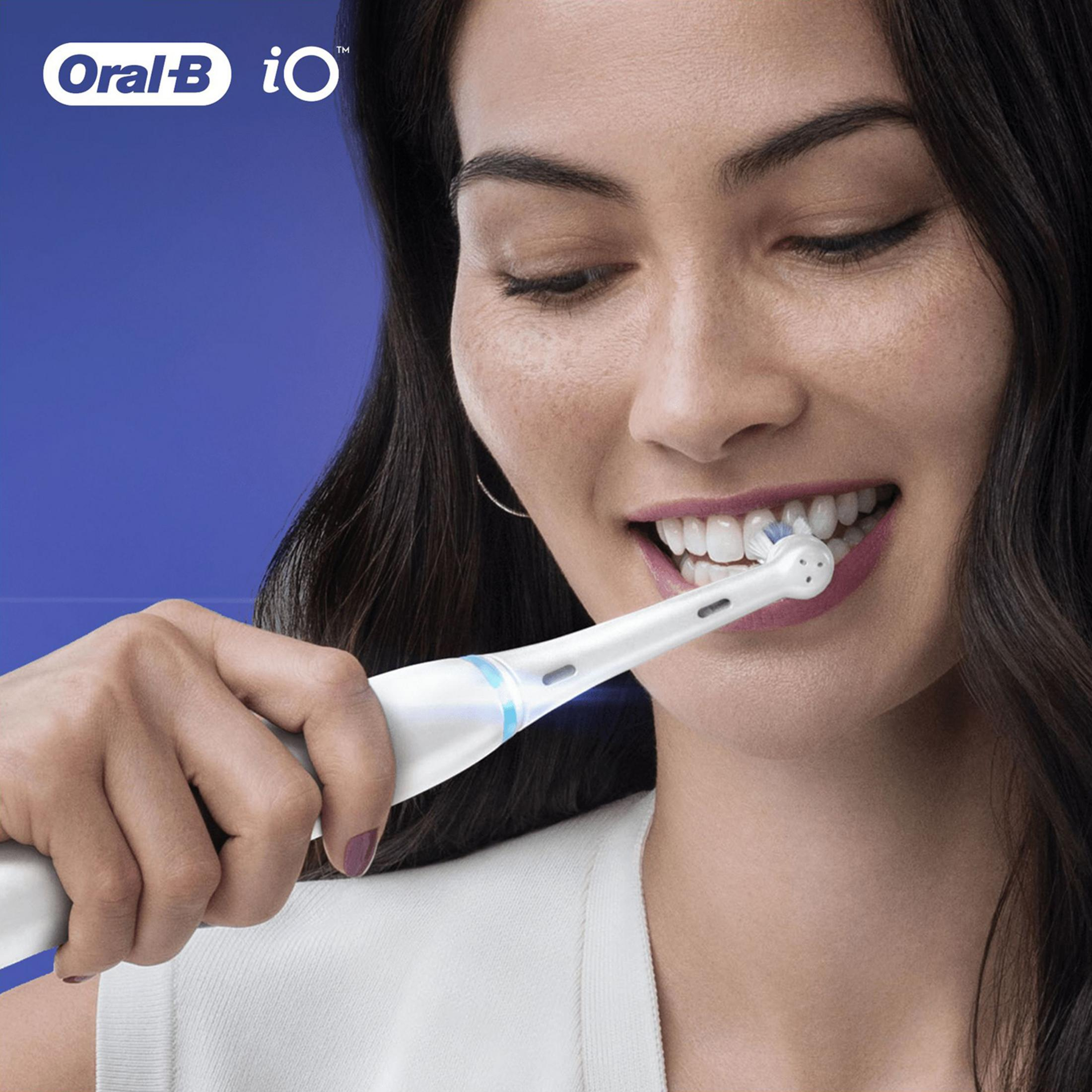 Mujer cepillándose los dientes con cepillo eléctrico blanco sobre fondo azul.