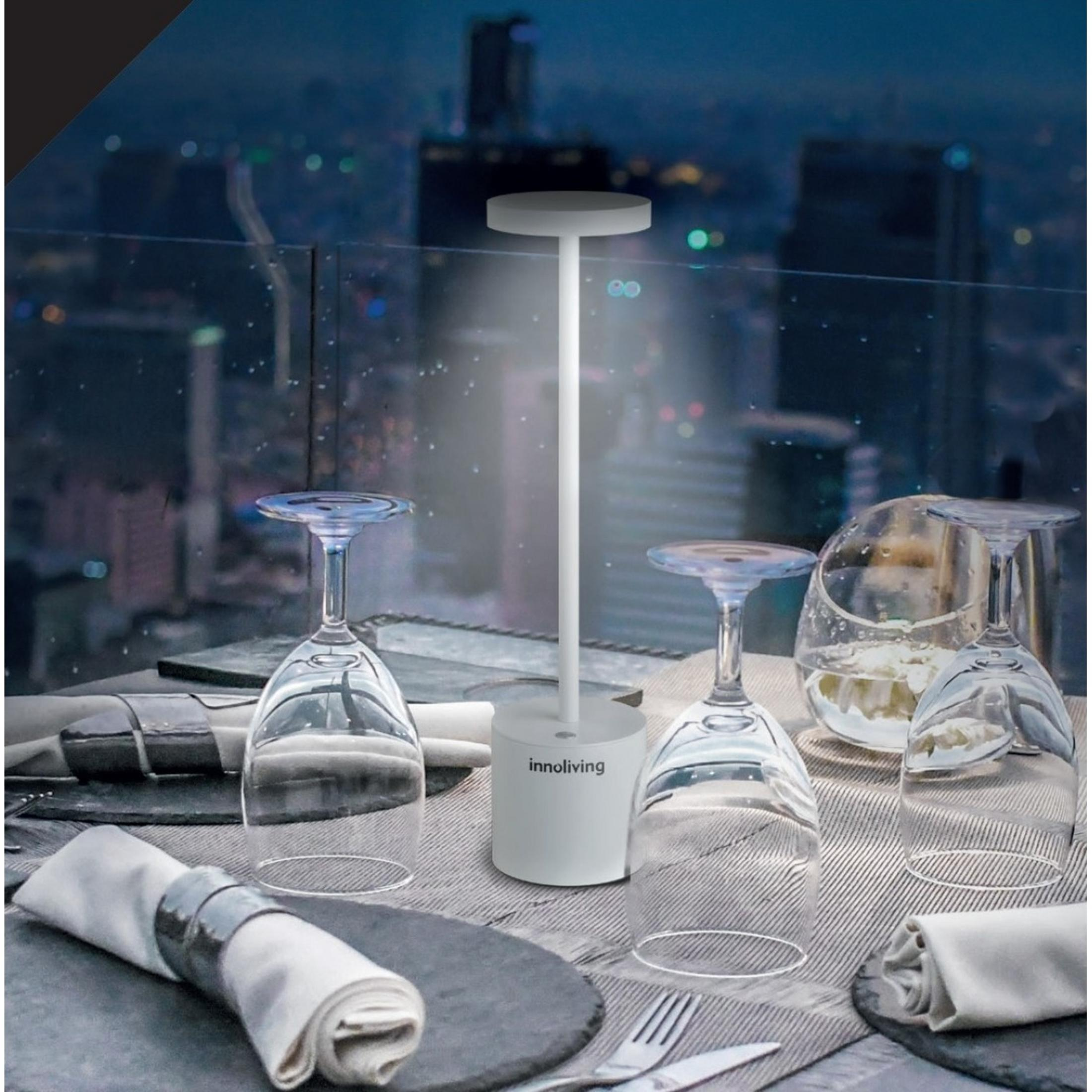 Un tavolo bianco con bicchieri e una lampada davanti a un paesaggio urbano notturno.