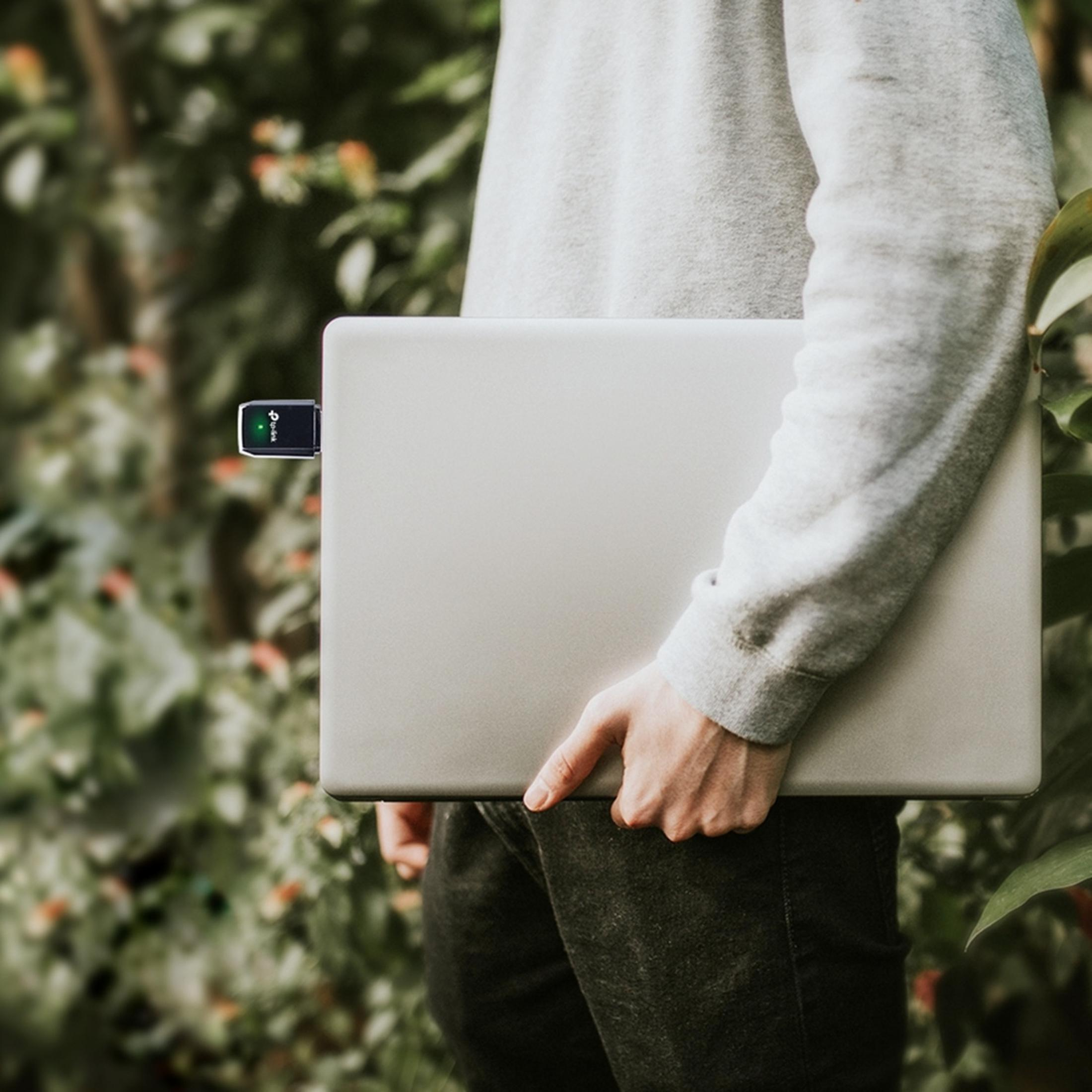 Osoba trzyma laptopa z kluczem Wi-Fi, na zewnątrz z zielenią.
