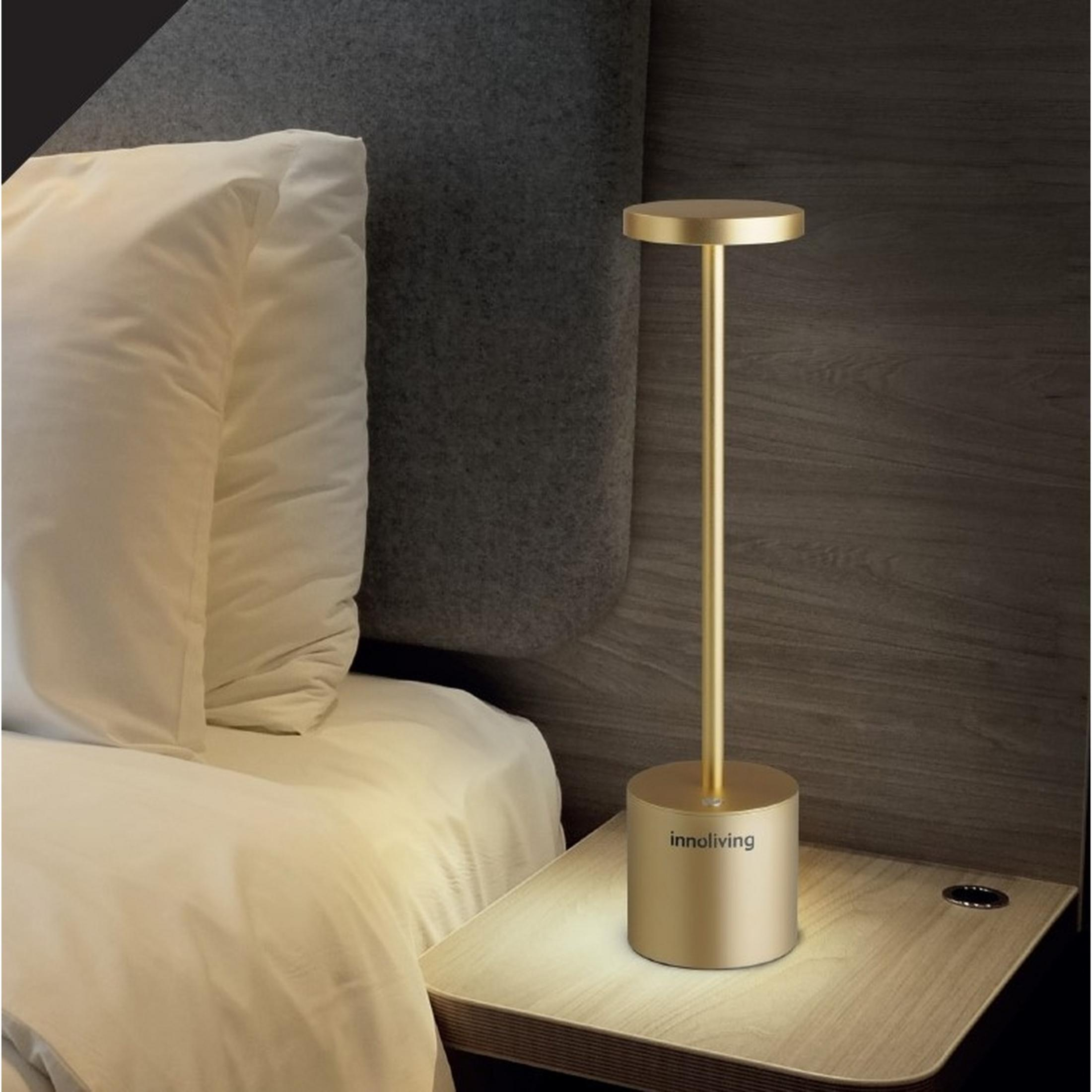 Una lampada da scrivania dorata è su un comodino accanto a un letto bianco.