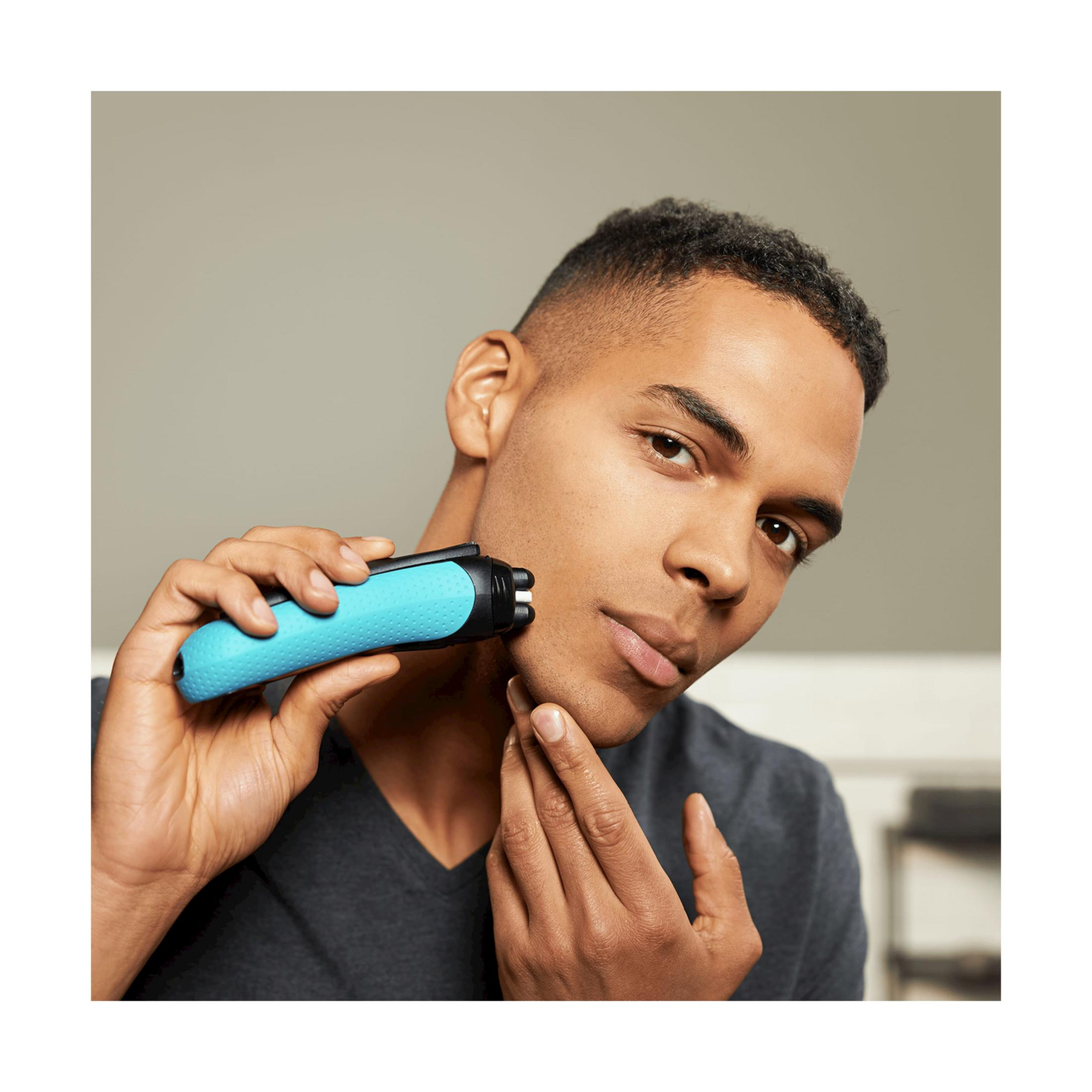 Mężczyzna goli twarz niebieską golarką elektryczną.