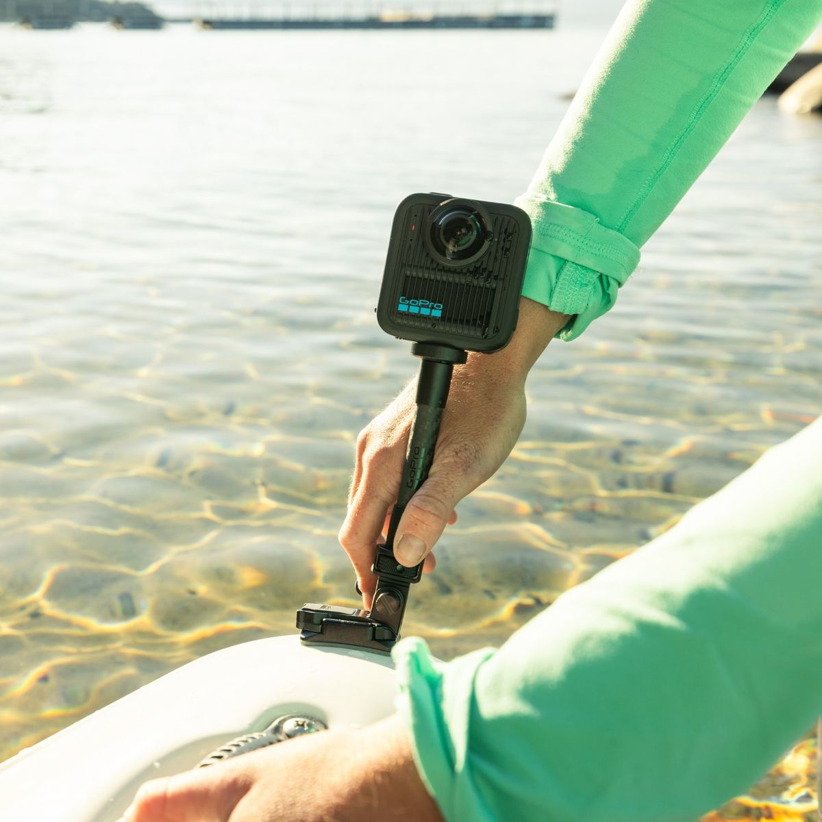 Hände halten eine GoPro-Kamera auf einem Stock über klarem Wasser. Unten ist ein weißes Objekt.
