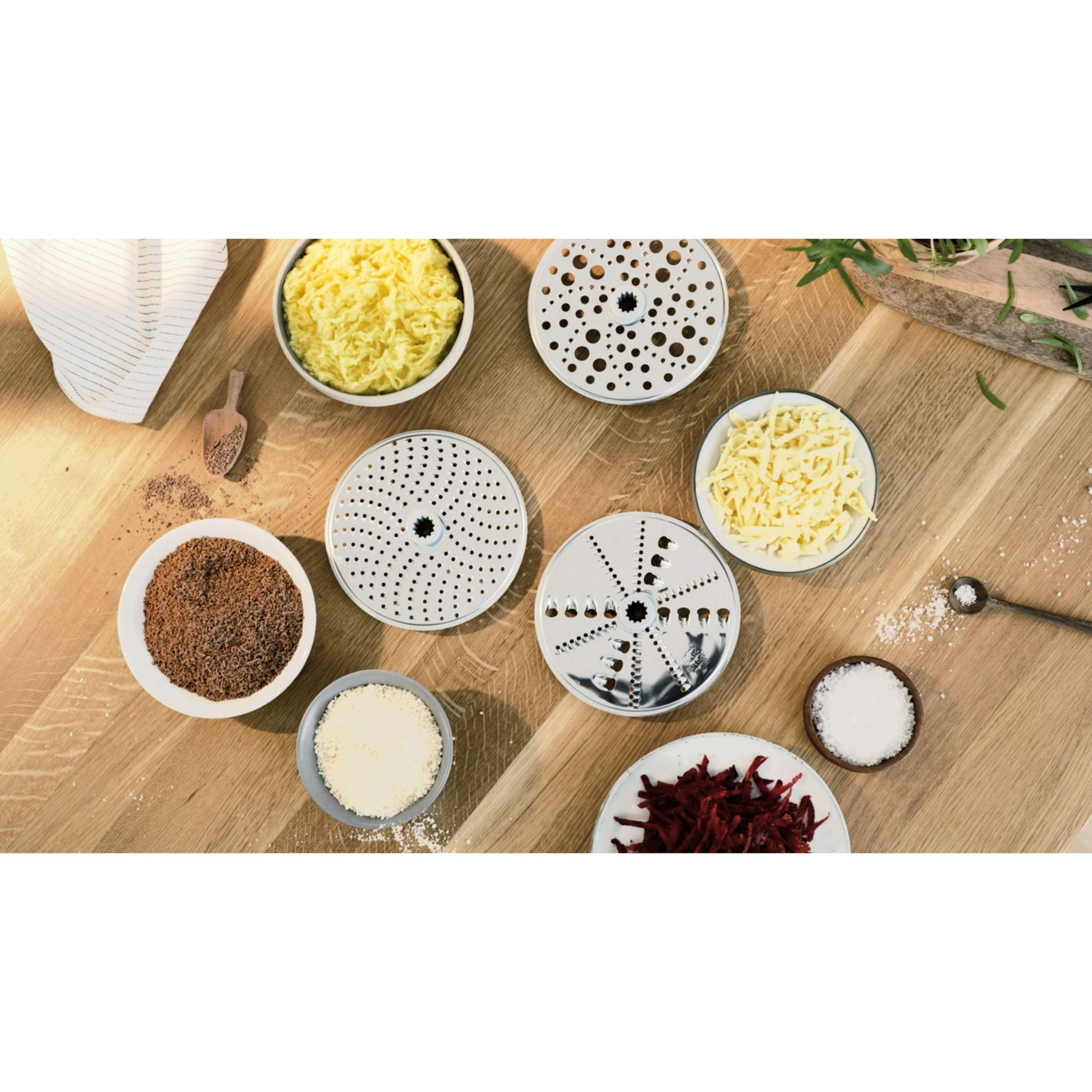 Vari dischi per grattugiare e ciotole con formaggio grattugiato, barbabietola, cioccolato e sale.