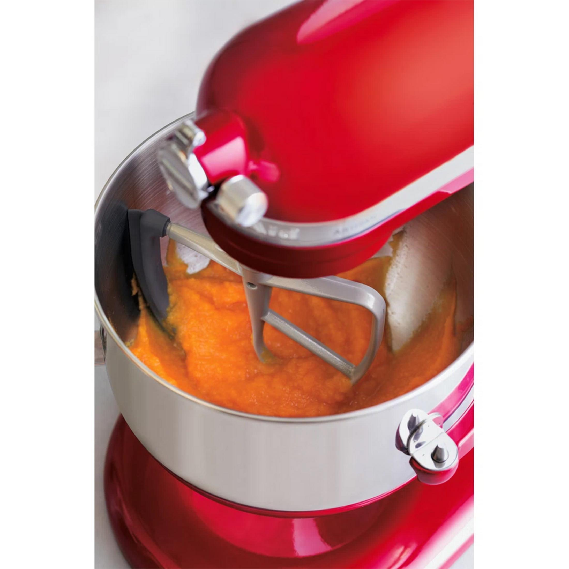 Ein roter Standmixer mit einem Flachrührer, der eine orangefarbene Masse in einer Edelstahlschüssel mixt.