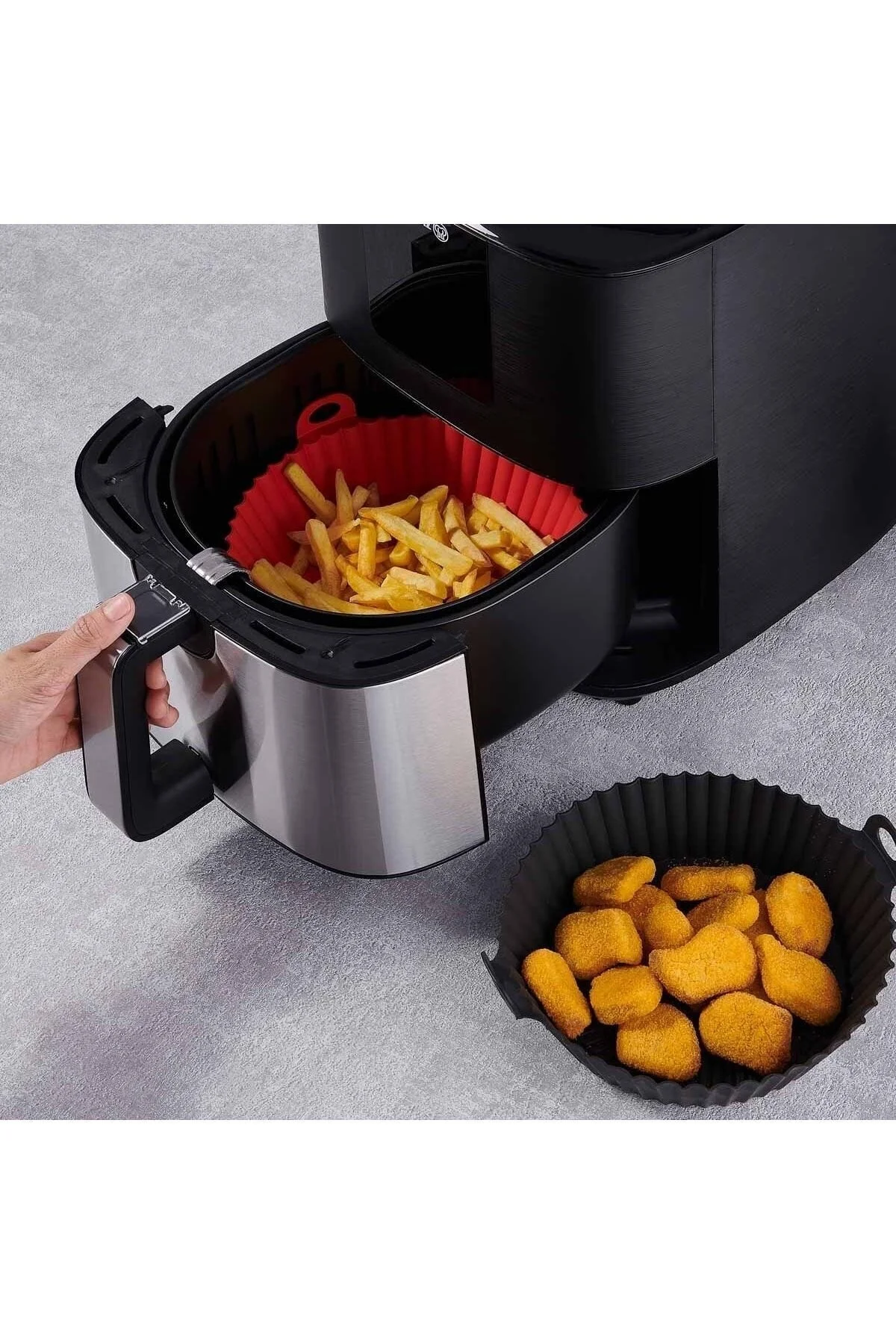Bir el, patates kızartmasıyla dolu bir fritöz sepetini çekiyor. Yanında nuggetlar var.