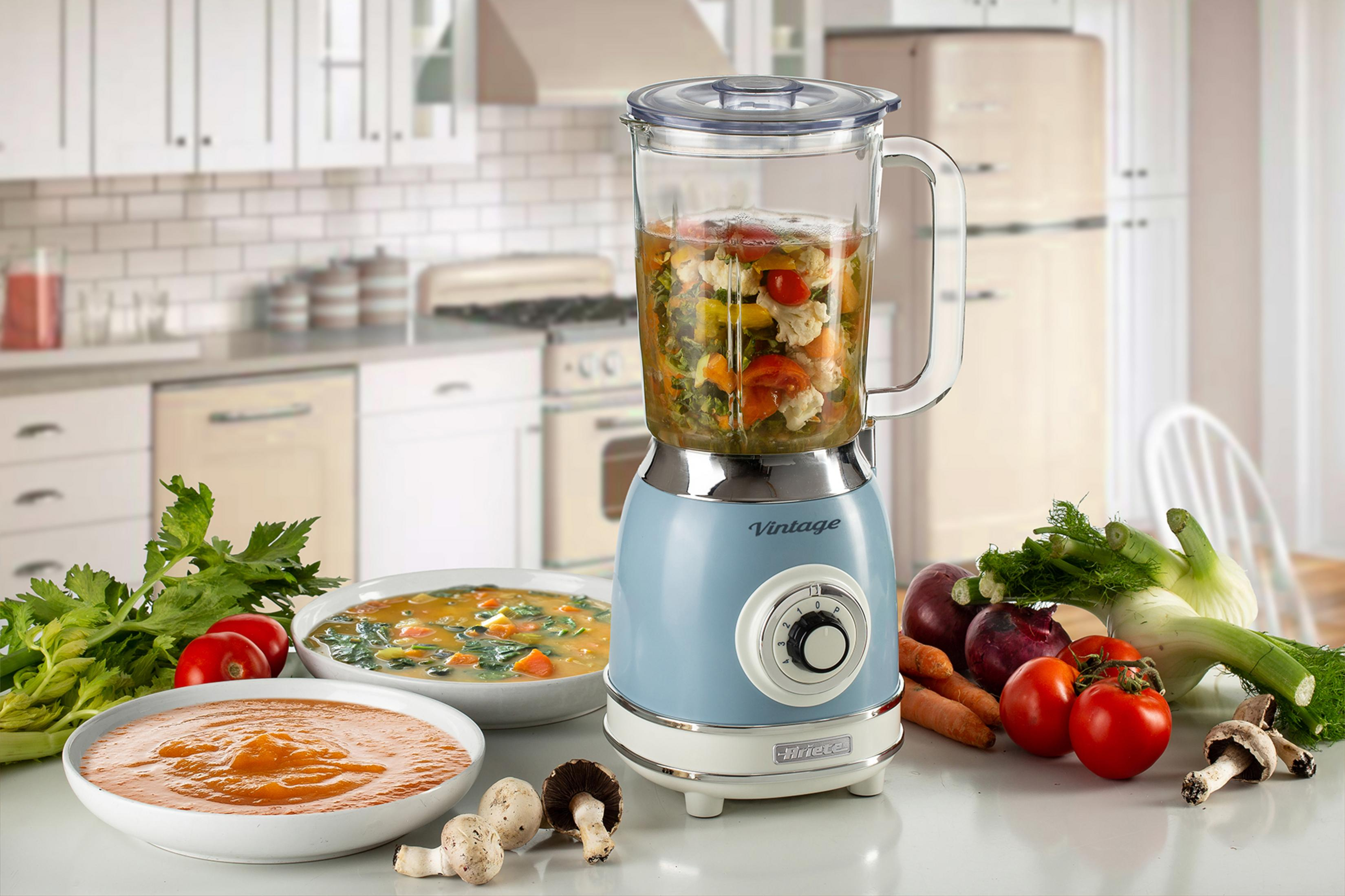 Een blauwe vintage blender op een keukenblad met ingrediënten en afgewerkte soepen.