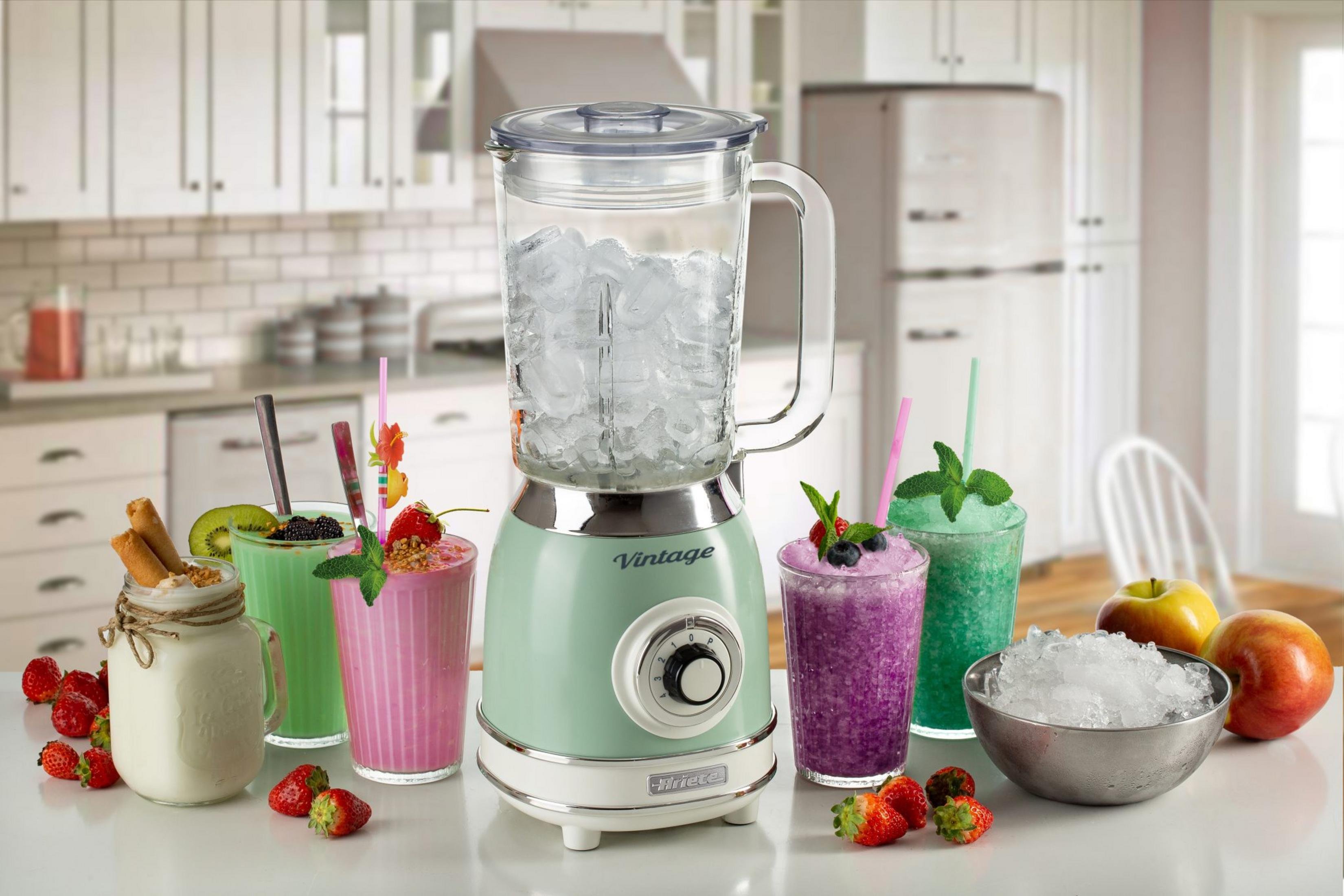 Een groene vintage blender gevuld met ijs, naast smoothies en fruit.